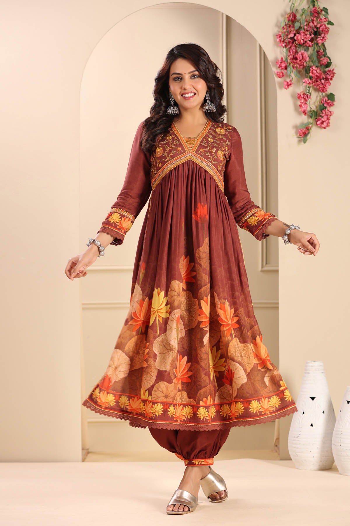 Woman wearing a brown traditional outfit with floral patterns in a decorated room.