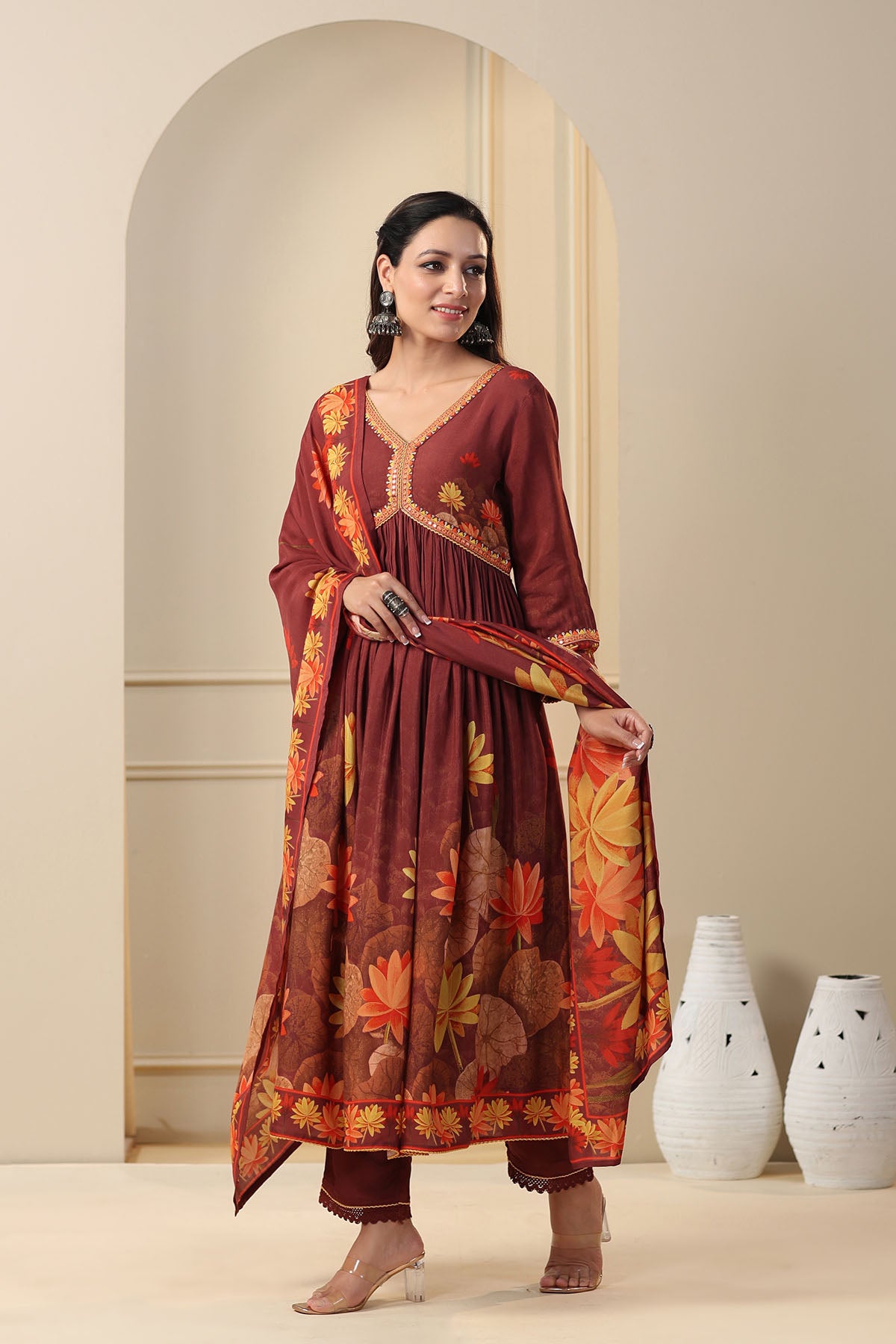 Woman wearing a maroon traditional outfit with floral patterns in a minimalistic setting.