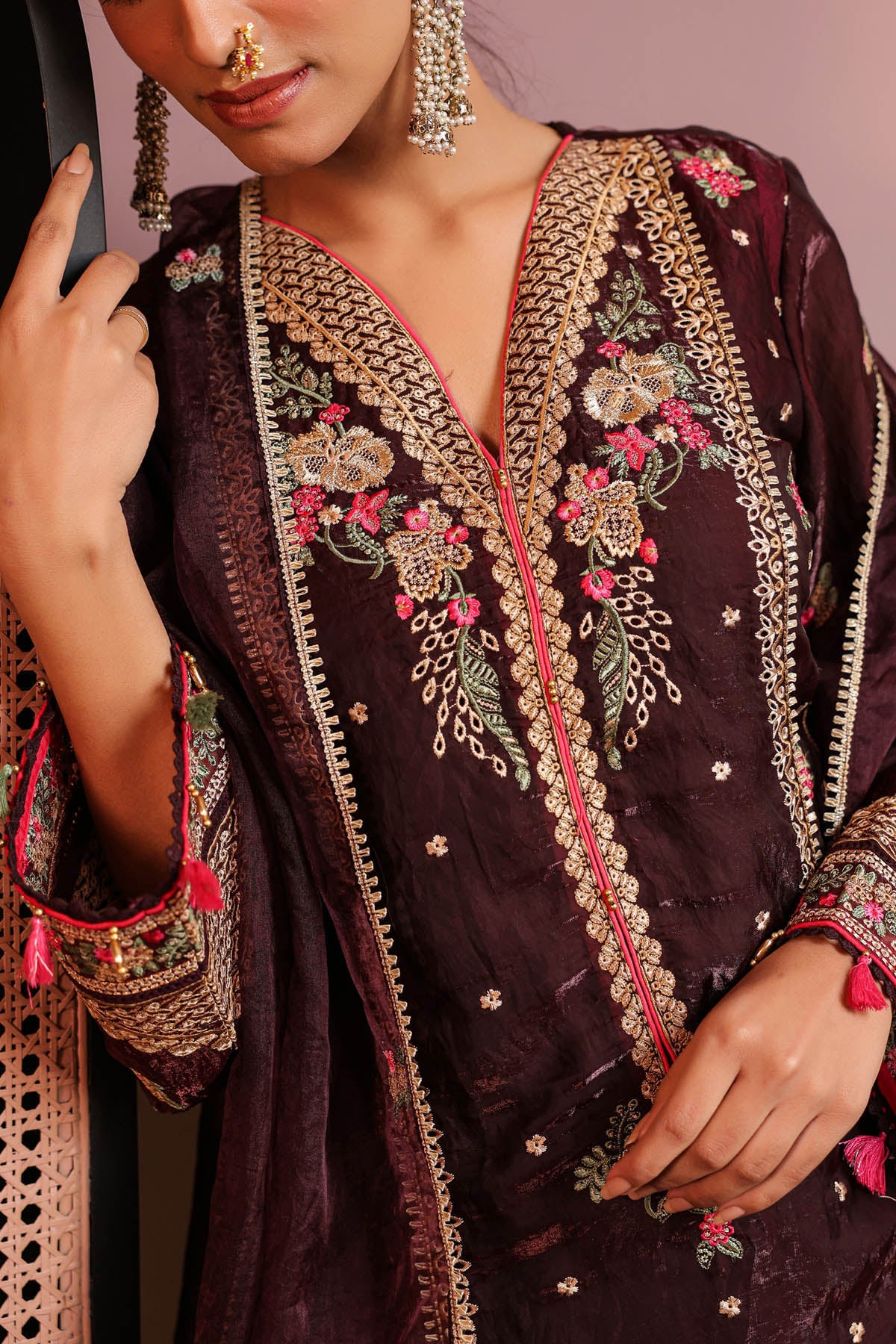 Woman wearing a dark purple embroidered traditional outfit with gold and pink details.