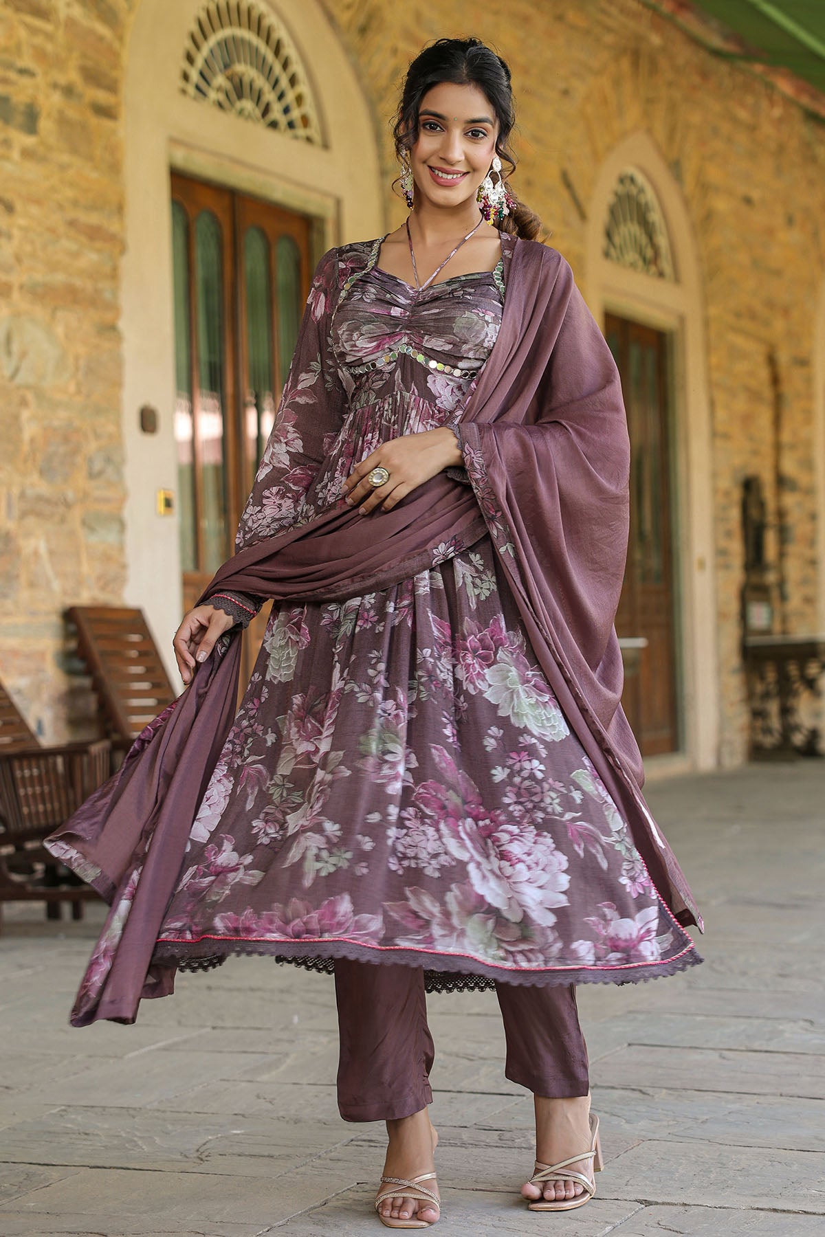 Woman in a floral dress with a matching dupatta standing in front of a stone building.