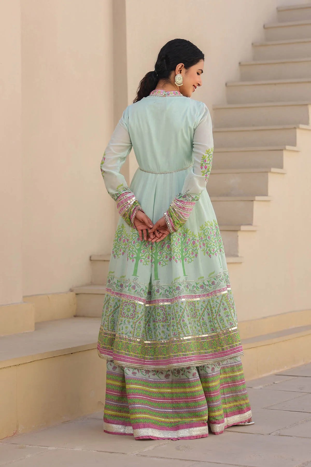 Woman in a light green traditional outfit with pink and white patterns standing on steps.