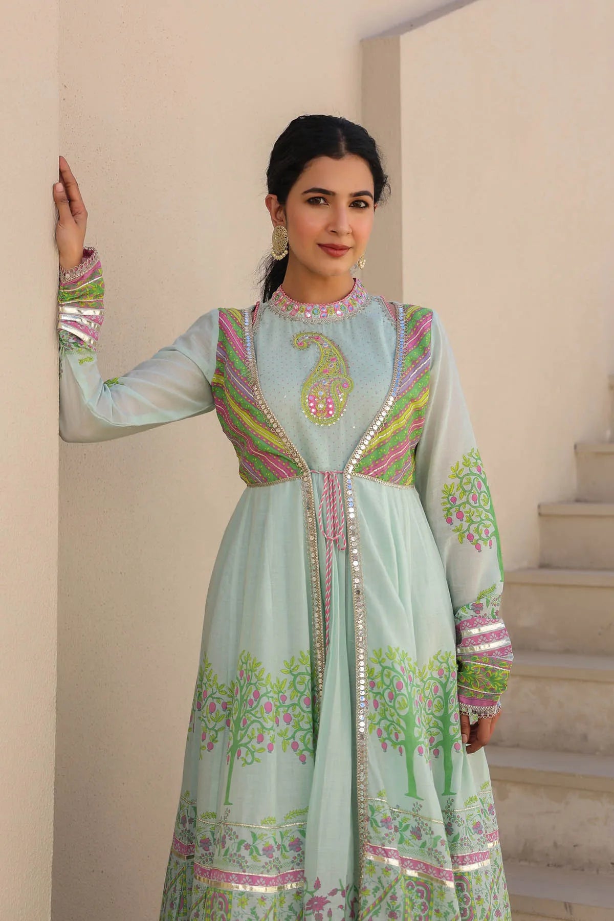 Woman wearing a light blue embroidered traditional outfit in an indoor setting.
