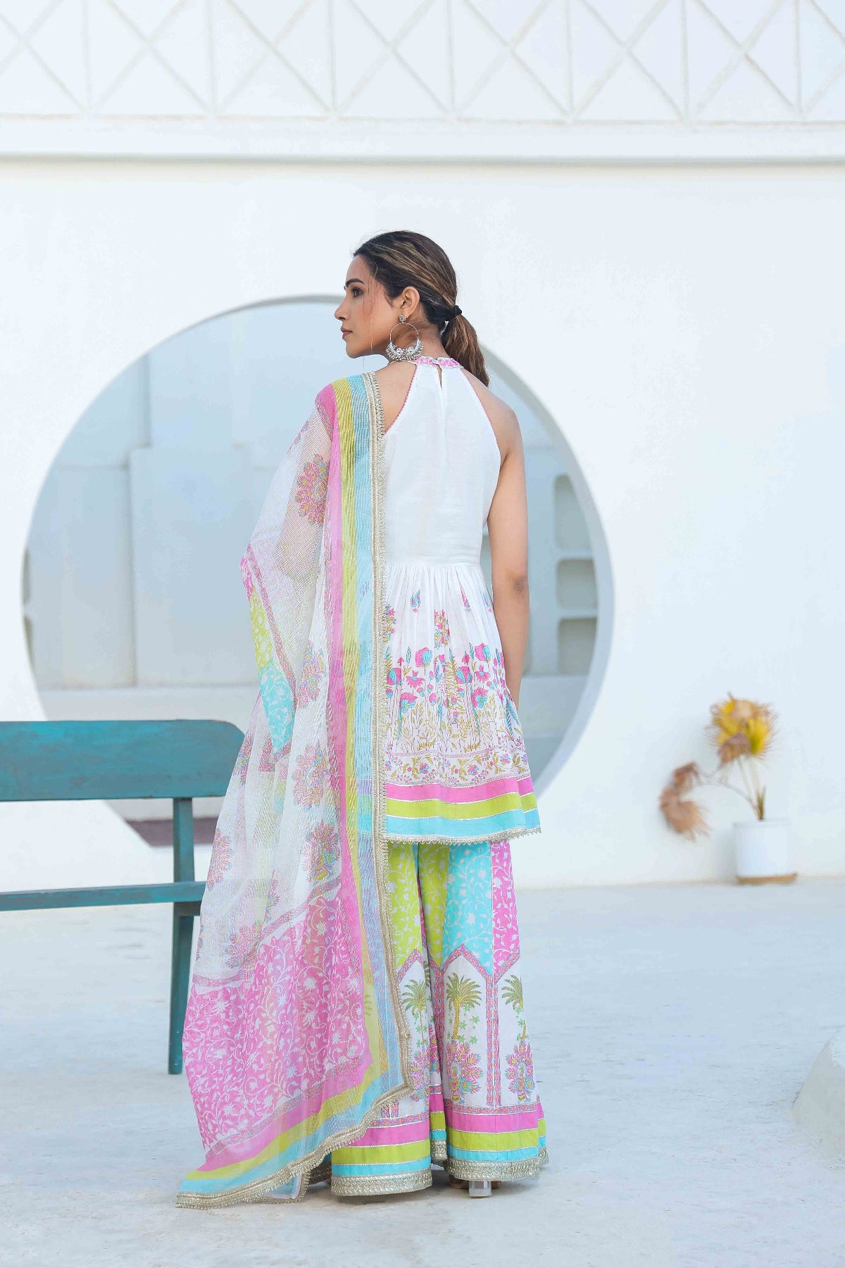 Woman in a colorful saree standing in a modern indoor setting.