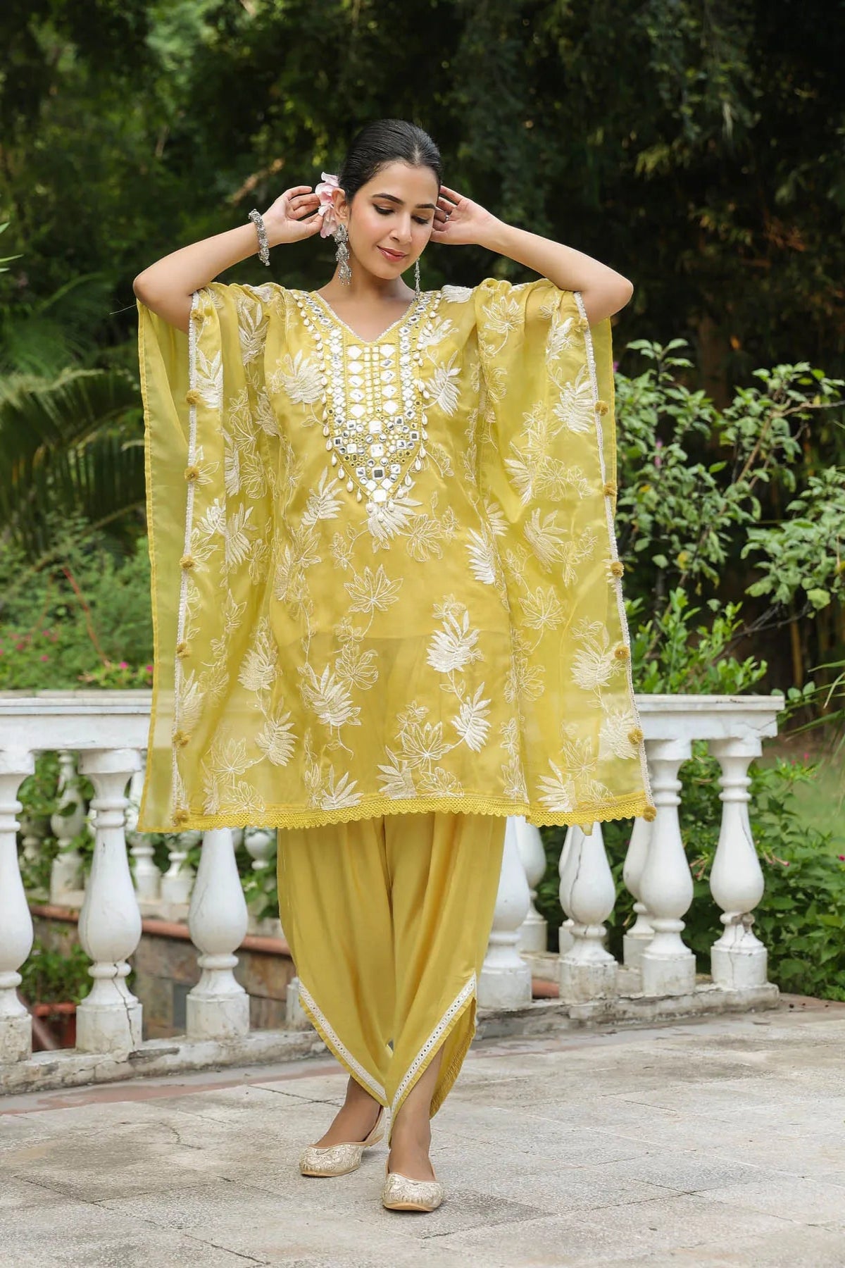 Woman in a yellow traditional outfit with white embroidery standing outdoors.