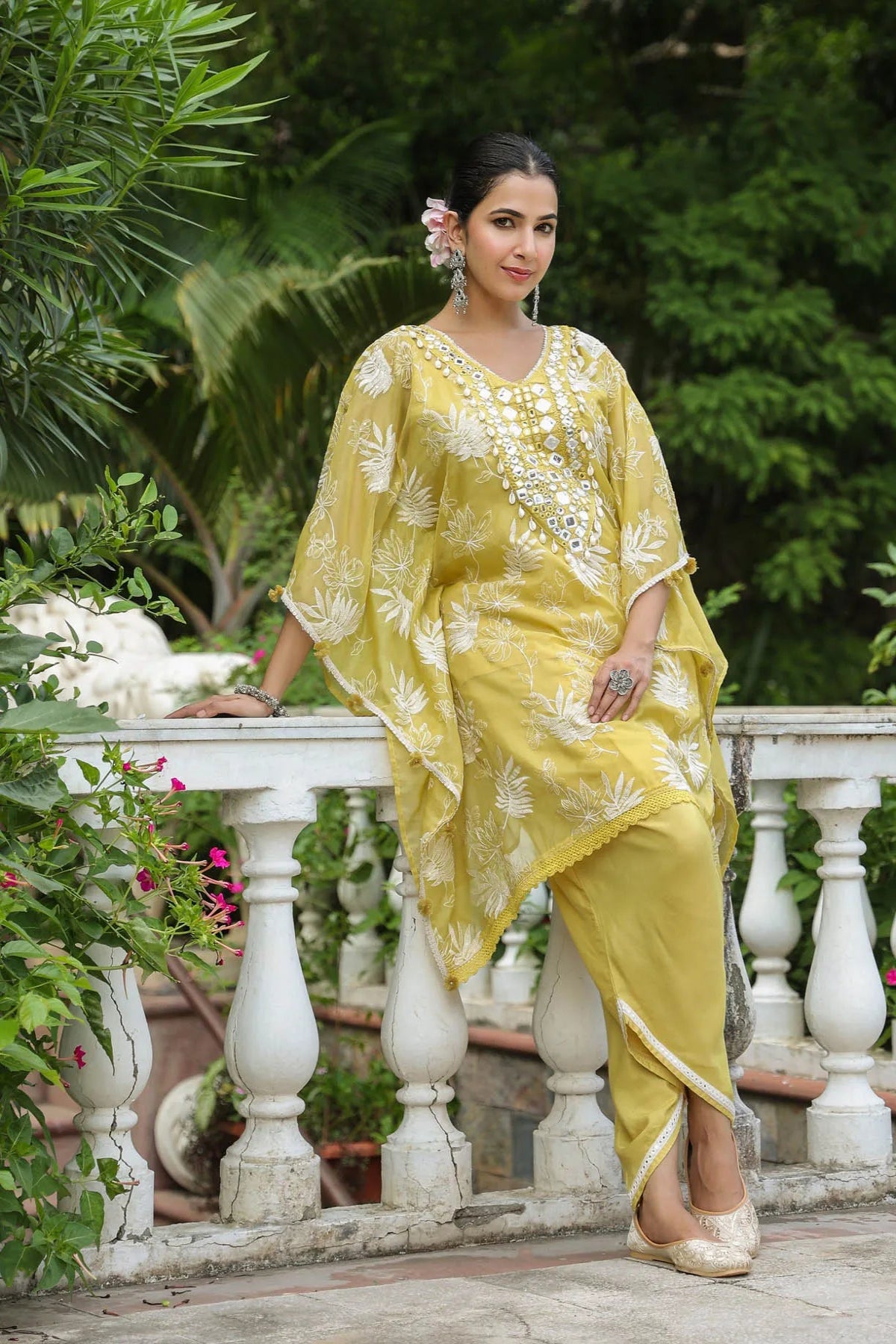 Woman in a yellow traditional outfit standing outdoors with greenery in the background