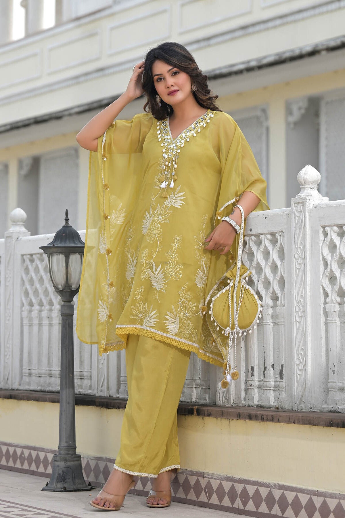 Woman in a yellow traditional outfit standing on a balcony with white railings.