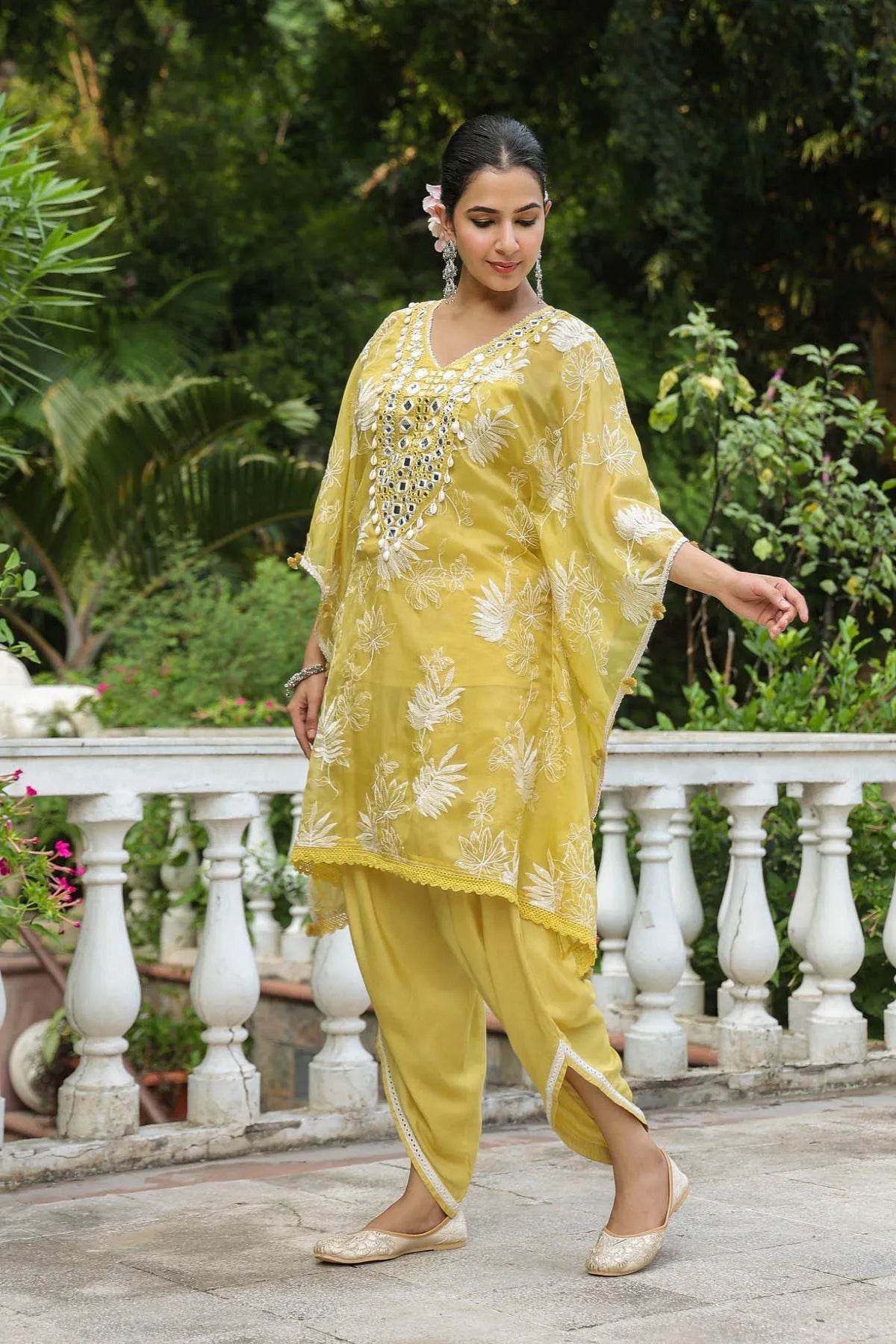 Woman in a yellow traditional outfit with floral patterns standing outdoors.