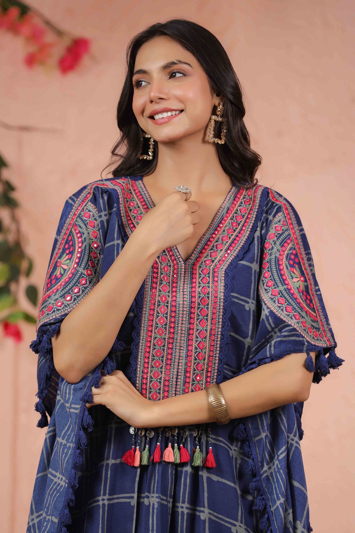 Woman wearing a blue embroidered dress with tassels against a pink background