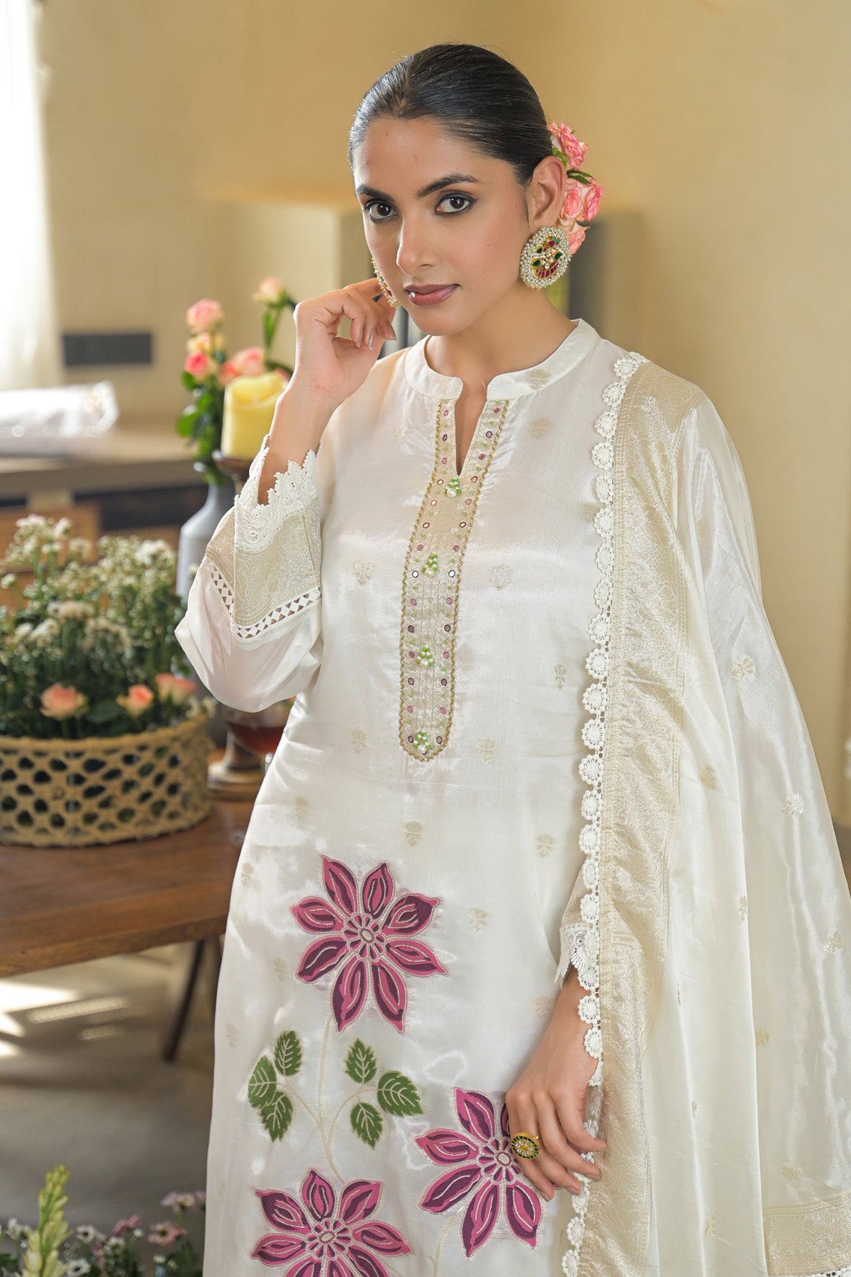 Woman wearing a white embroidered outfit with pink floral patterns in an indoor setting.