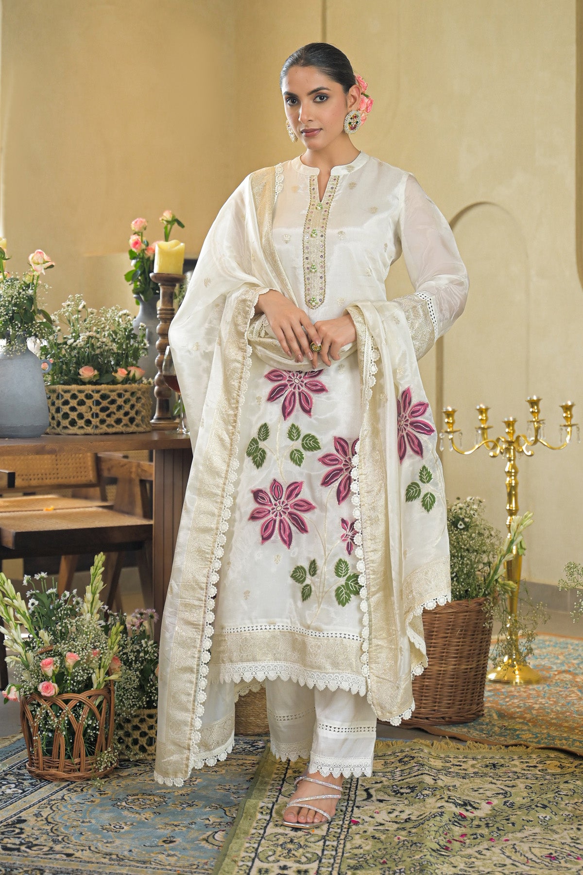 Woman in a white traditional outfit with floral patterns in a decorated room.