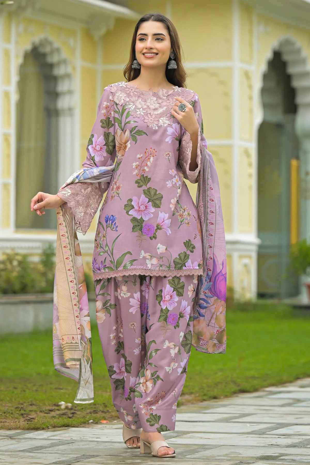 Woman wearing a pink floral outfit standing outdoors with classical architecture in the background