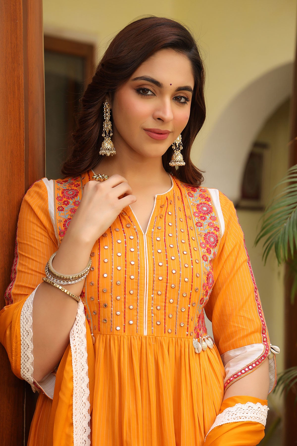 Woman wearing an orange traditional outfit with floral patterns indoors.
