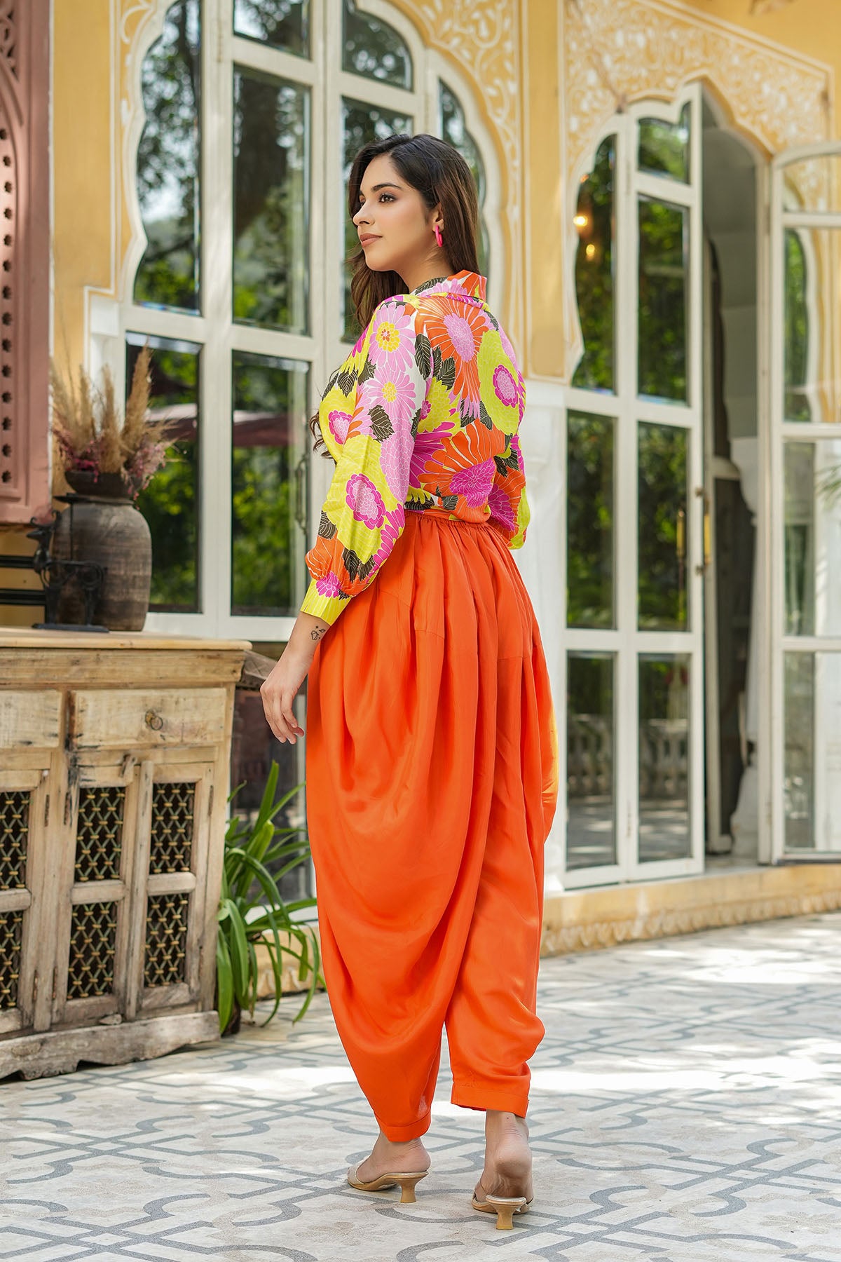 Woman in colorful outfit standing in front of a decorative building with large windows.