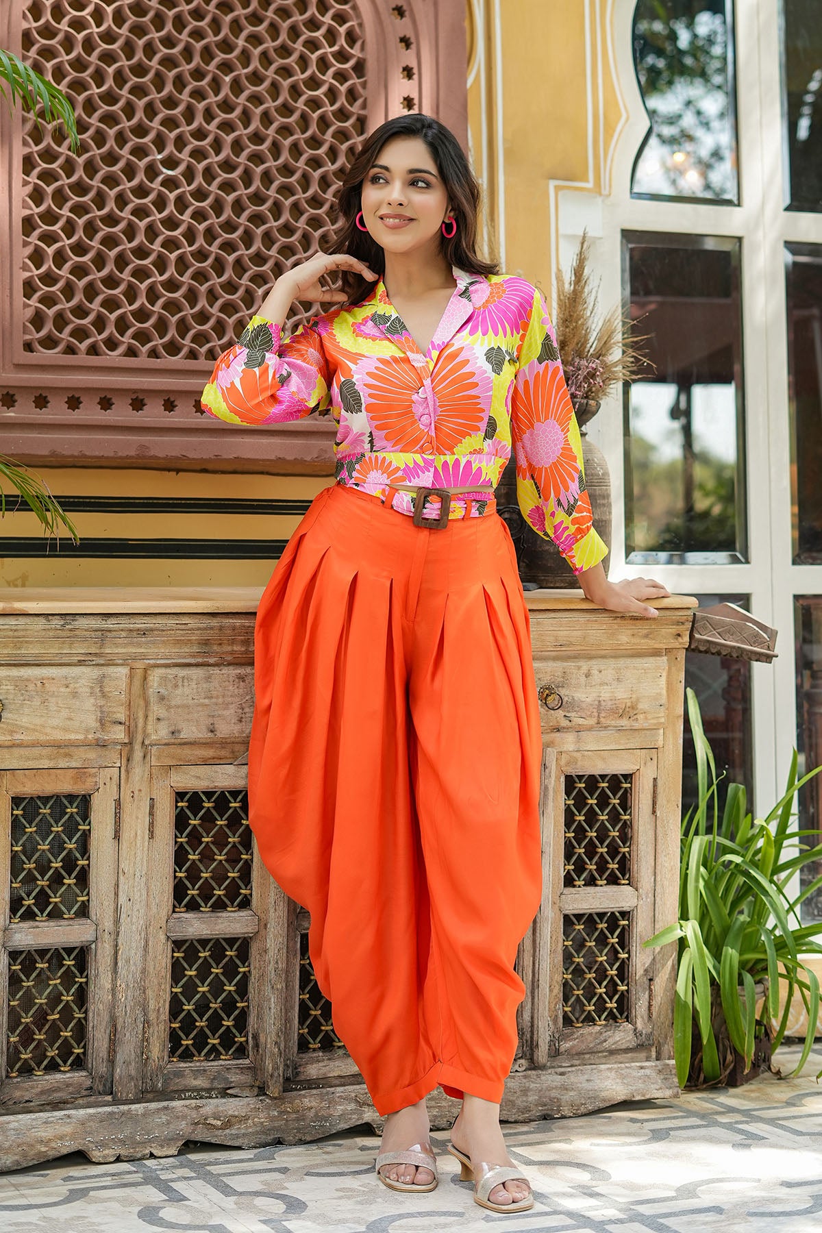 Woman in colorful top and orange dhoti standing in front of a wooden cabinet.