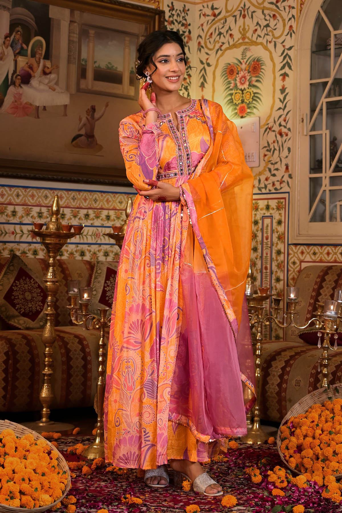 Woman in a colorful traditional outfit standing in an ornate decorated room.