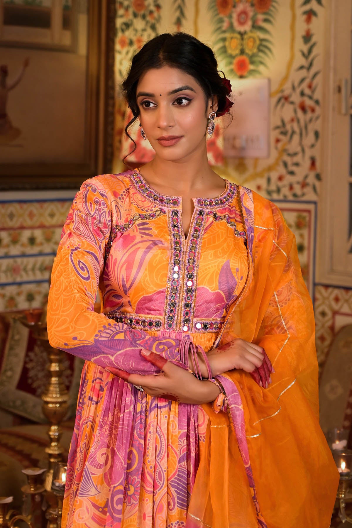 Woman in a colorful traditional outfit standing in an ornate room.