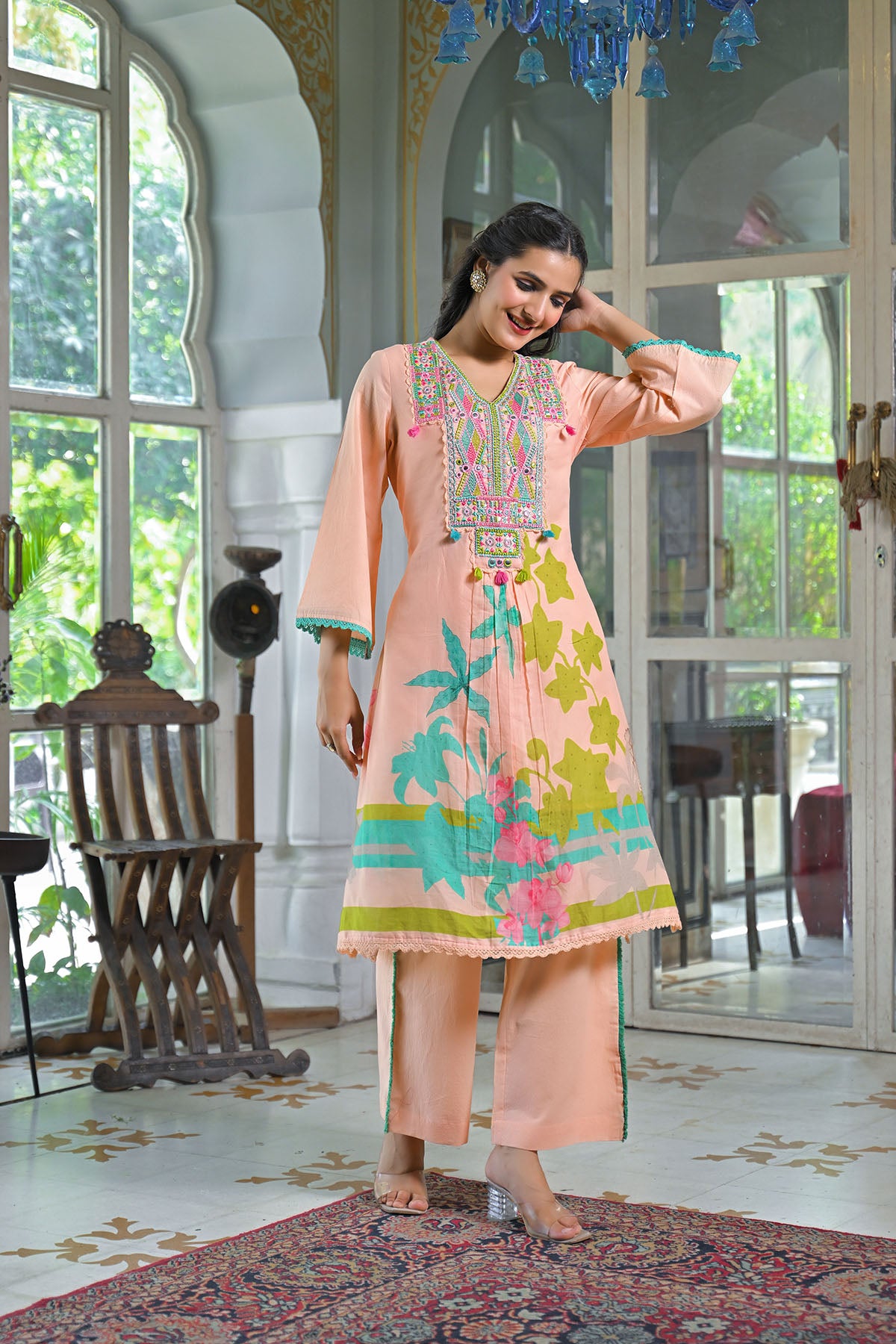Woman in a colorful traditional outfit standing in a decorated room with large windows.