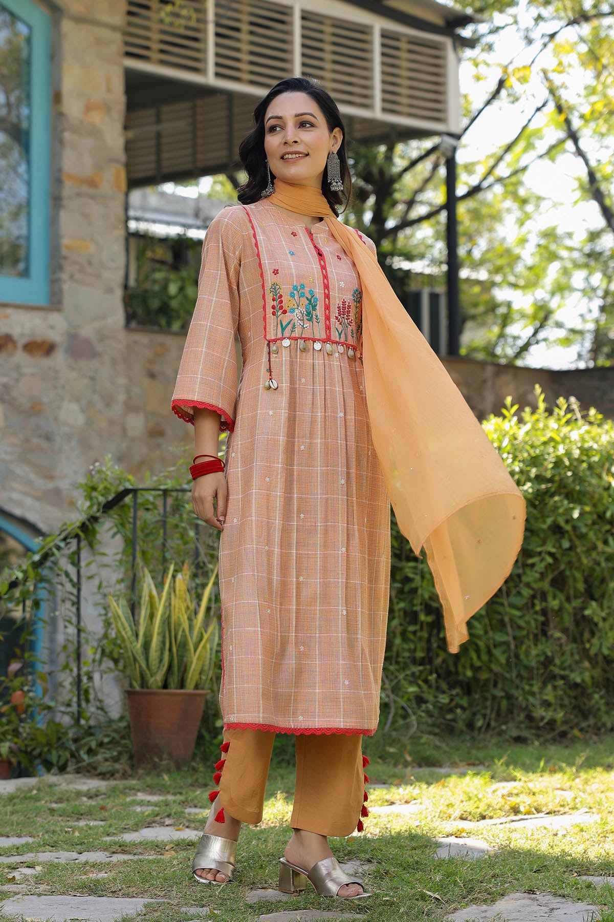 Woman in traditional outfit with embroidered top and checkered skirt standing outdoors.