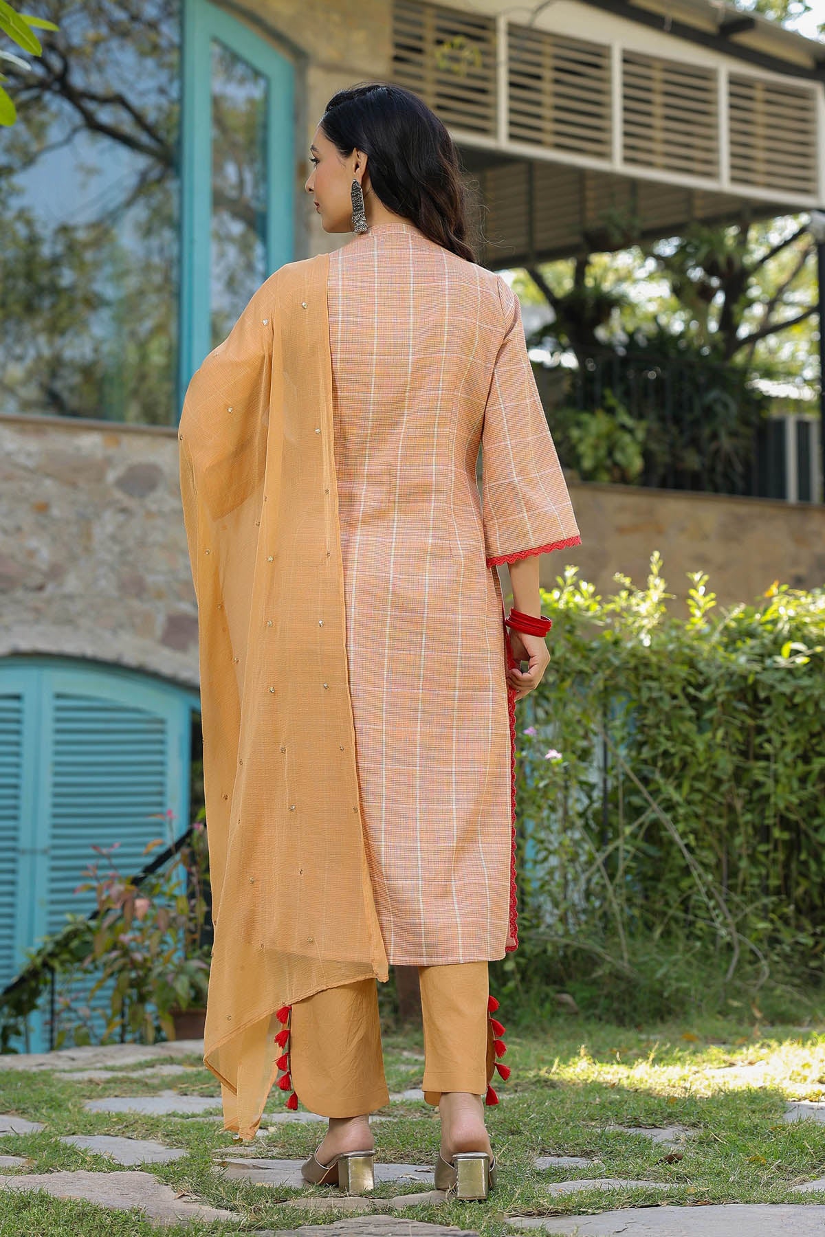 Woman in a traditional outfit standing outdoors with a building and greenery in the background