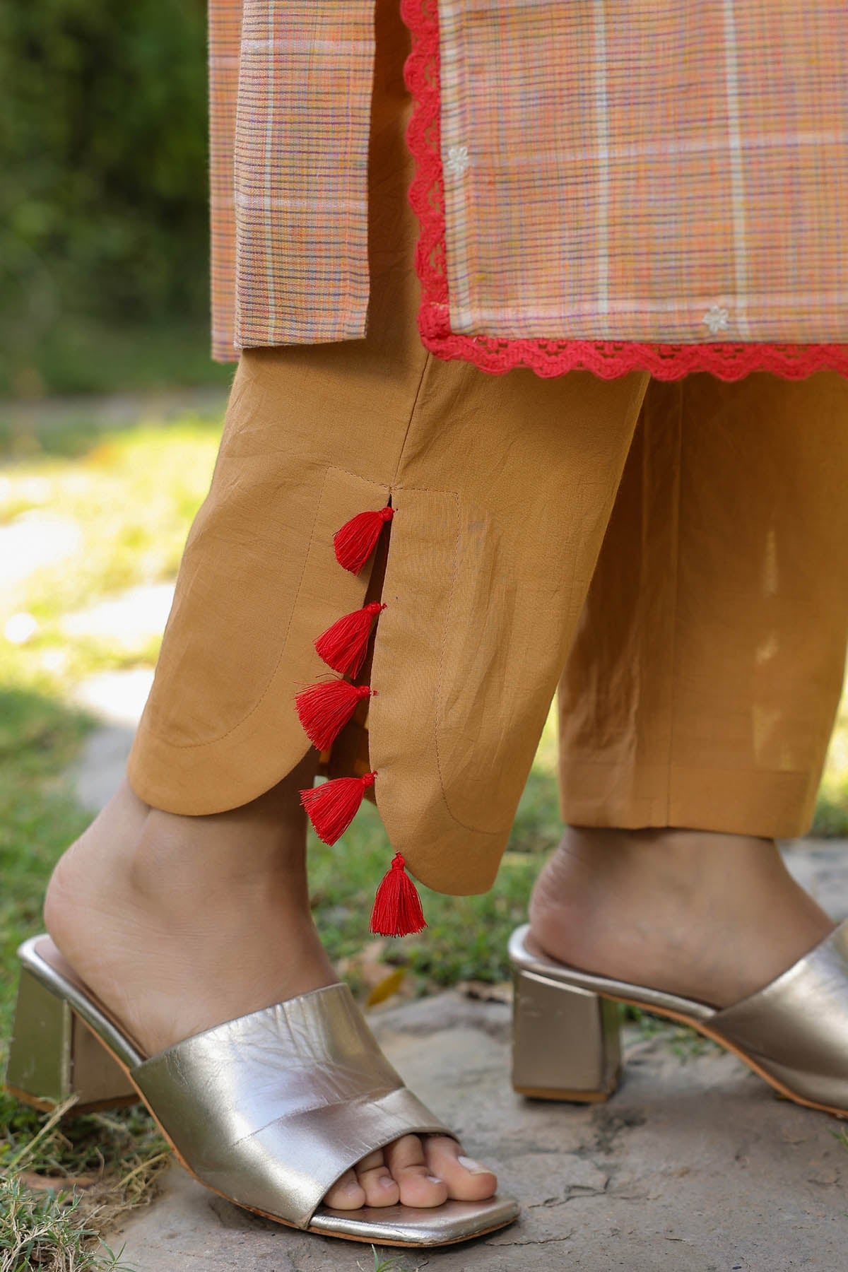 Person wearing mustard yellow pants with red tassels and gold high-heeled sandals outdoors.