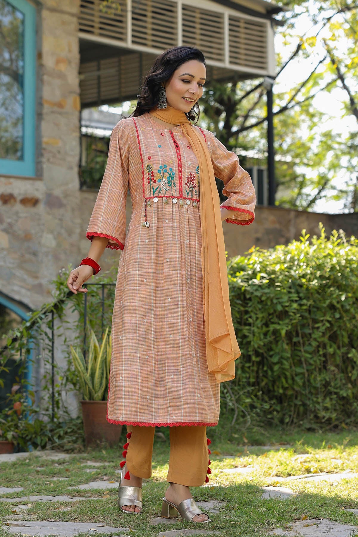 Woman wearing a peach-colored embroidered kurta with a matching dupatta in an outdoor setting.
