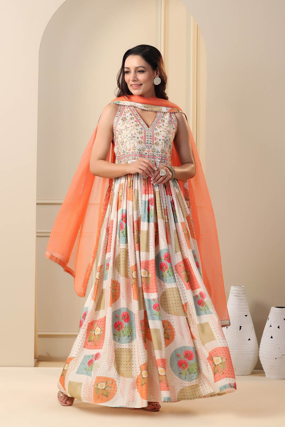 Woman wearing a floral dress with an orange dupatta in a neutral setting