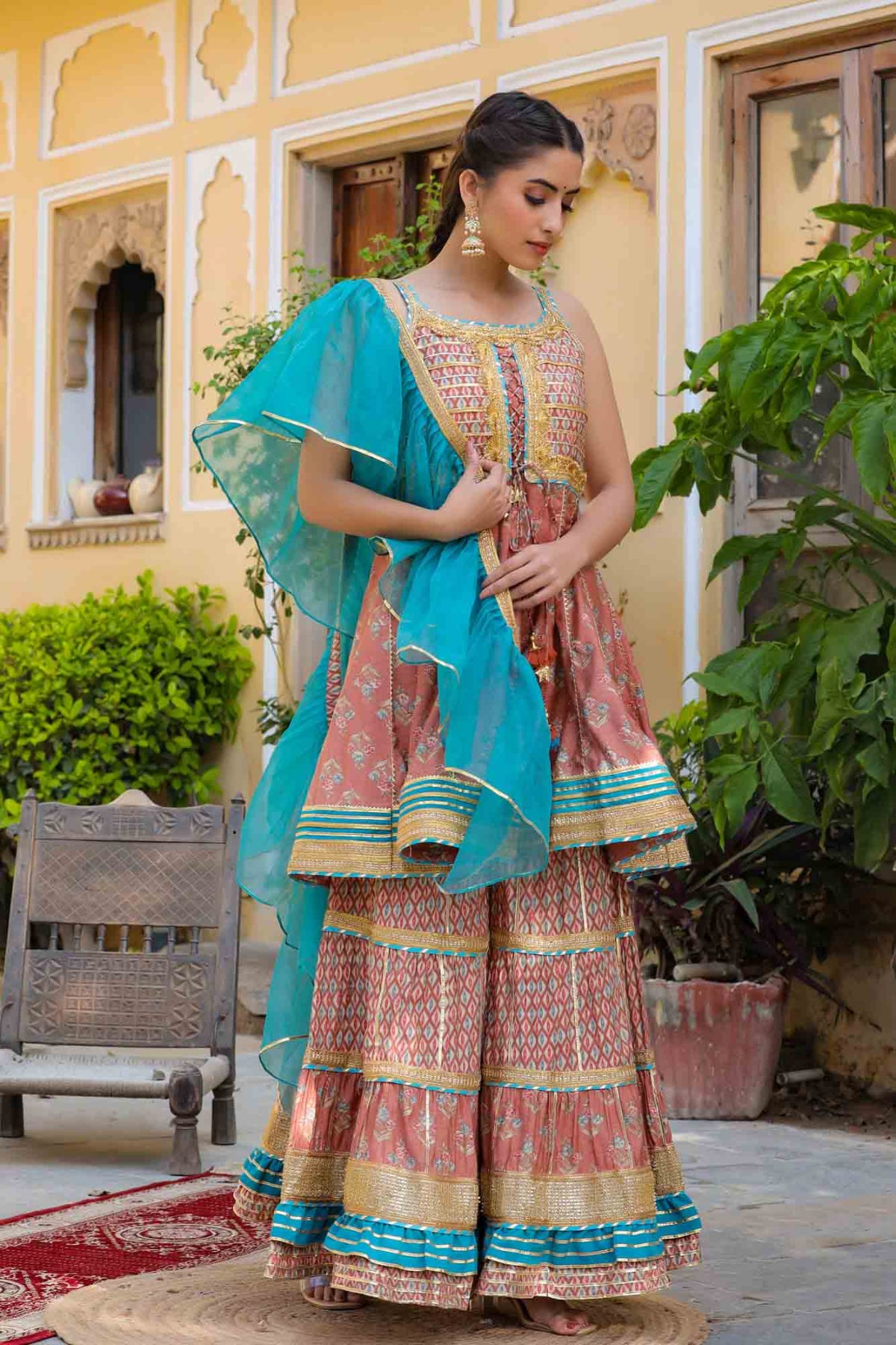 Woman in traditional outfit with turquoise dupatta standing outdoors.