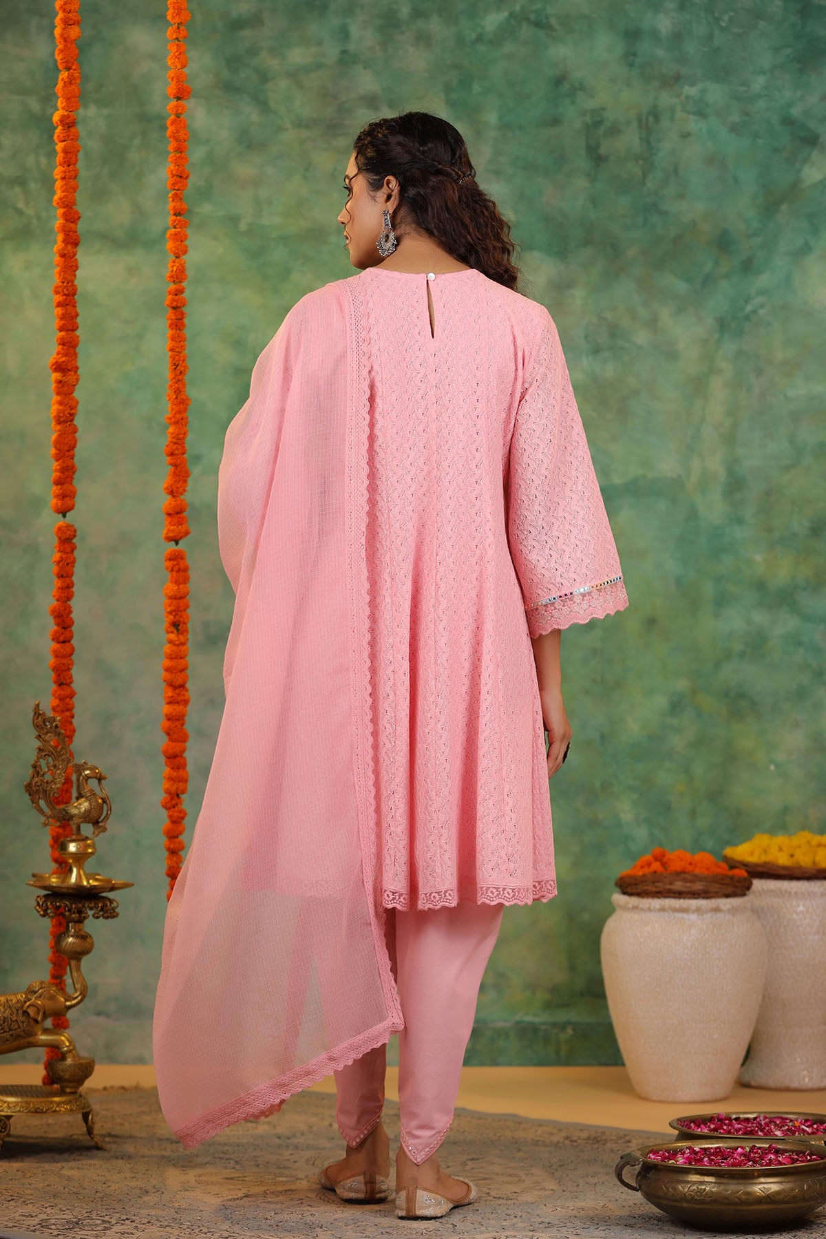 Woman in a pink traditional outfit standing against a green wall with decorative elements.