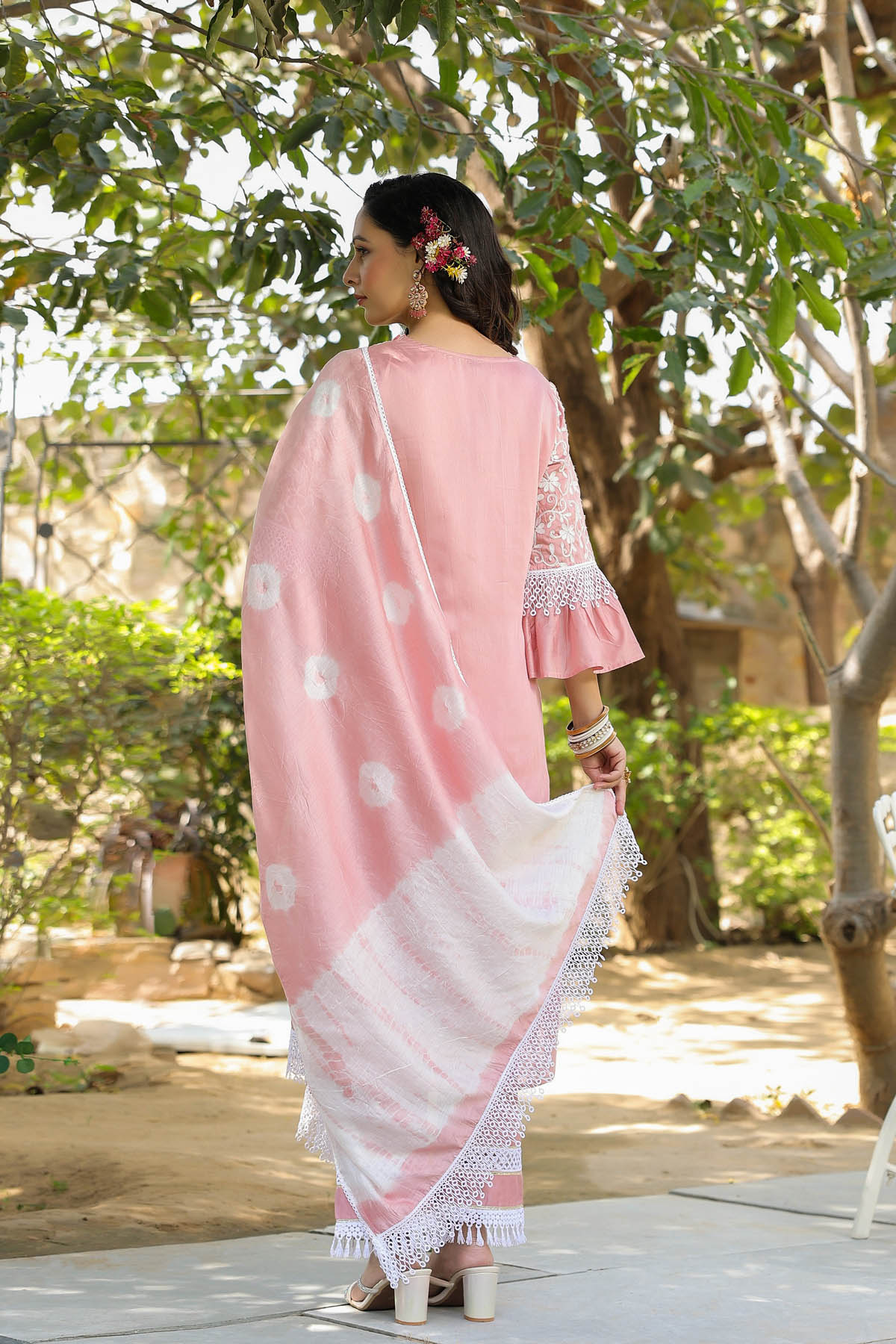 Woman in a pink and white traditional outfit standing outdoors with trees in the background