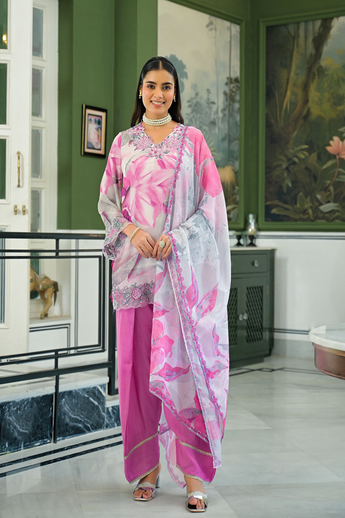 Woman in a pink and white floral outfit standing in a stylish interior setting.