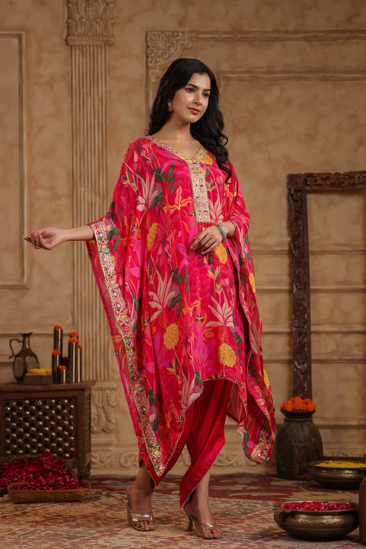 Woman in a bright pink traditional outfit with floral patterns in an ornate room.