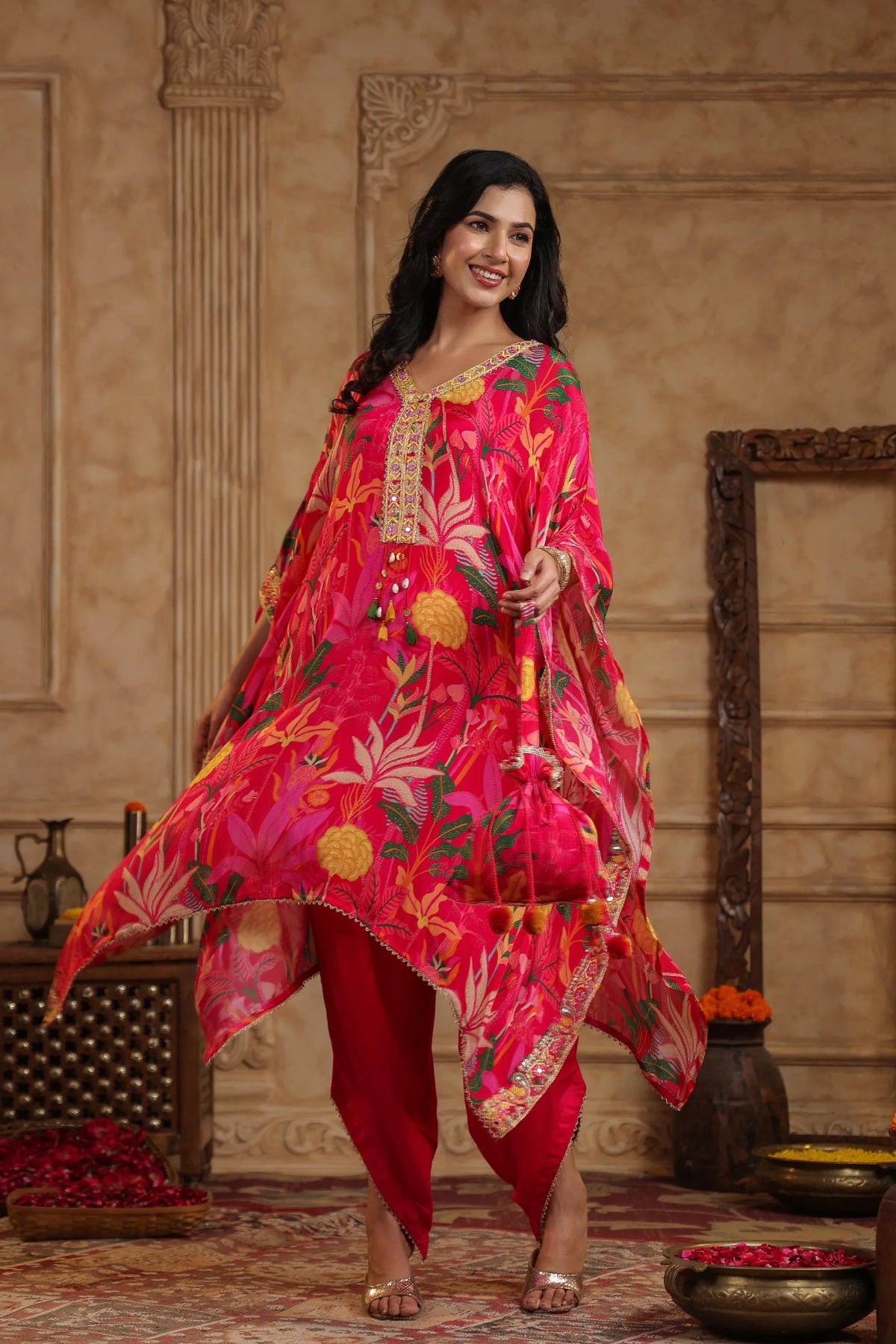 Woman in a vibrant pink and red traditional outfit with floral patterns in an ornate room.