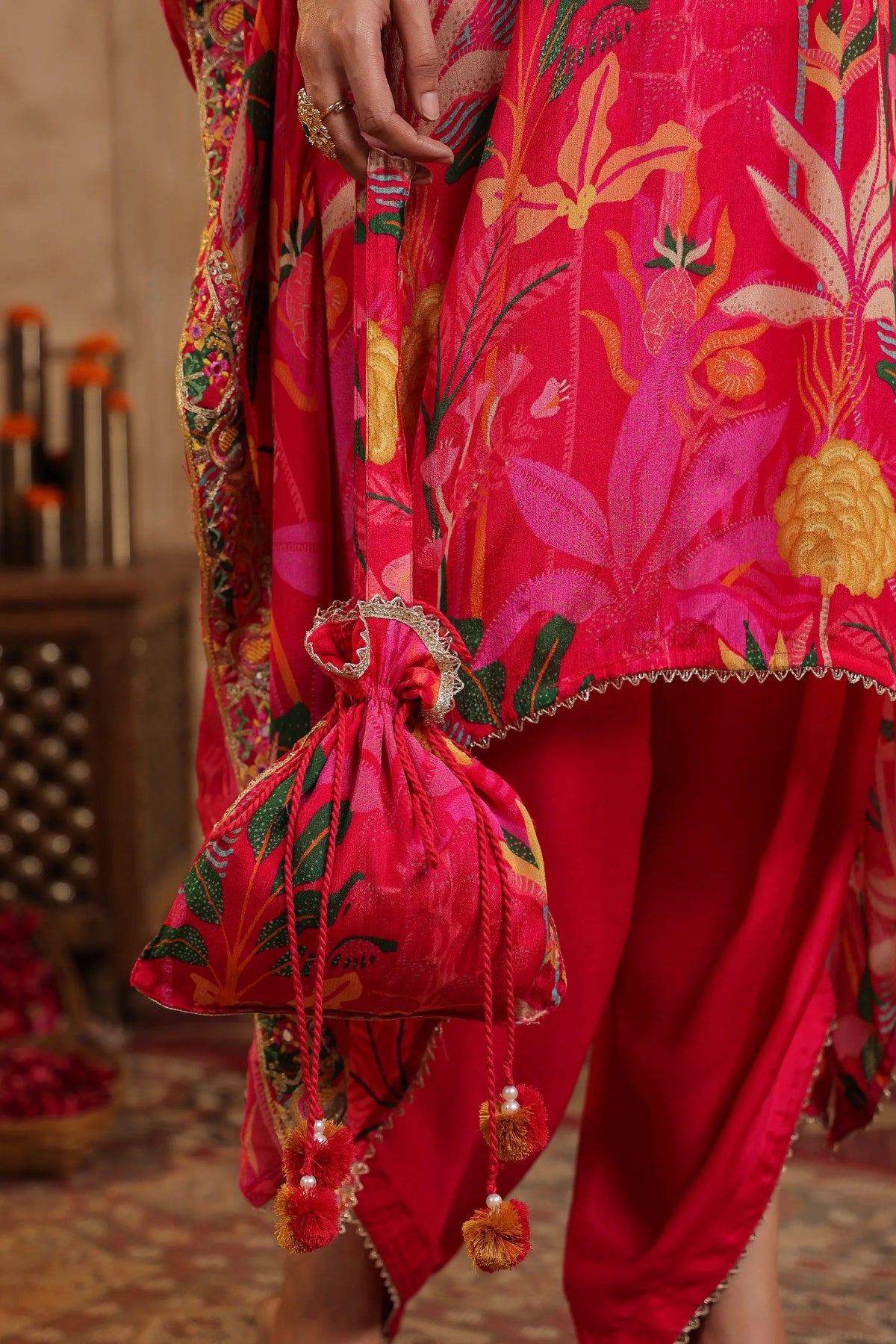 Person wearing a vibrant red traditional outfit with floral patterns, holding a matching bag.