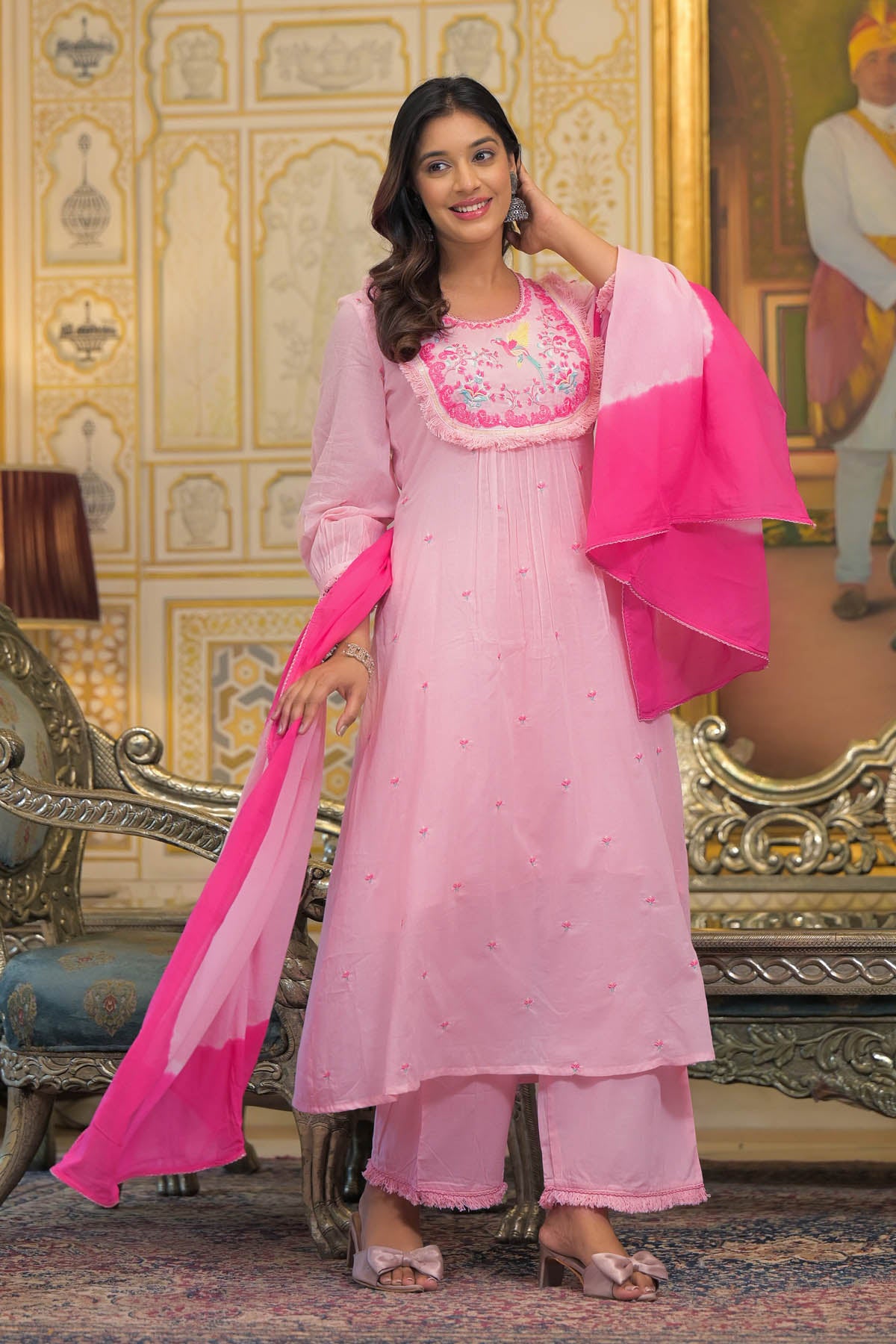 Woman in a pink traditional outfit with embroidery in a decorated room.