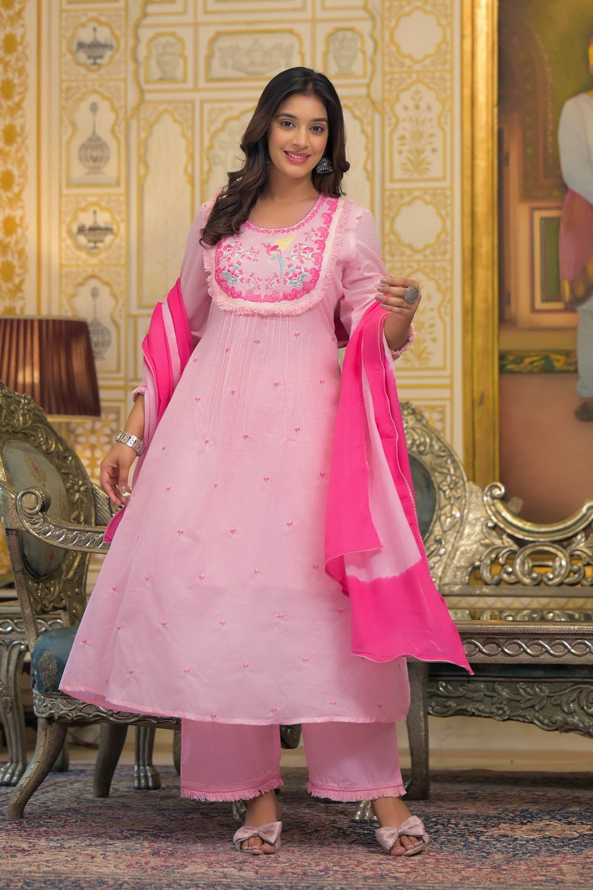 Woman in a pink traditional outfit with a matching dupatta in a decorated room.