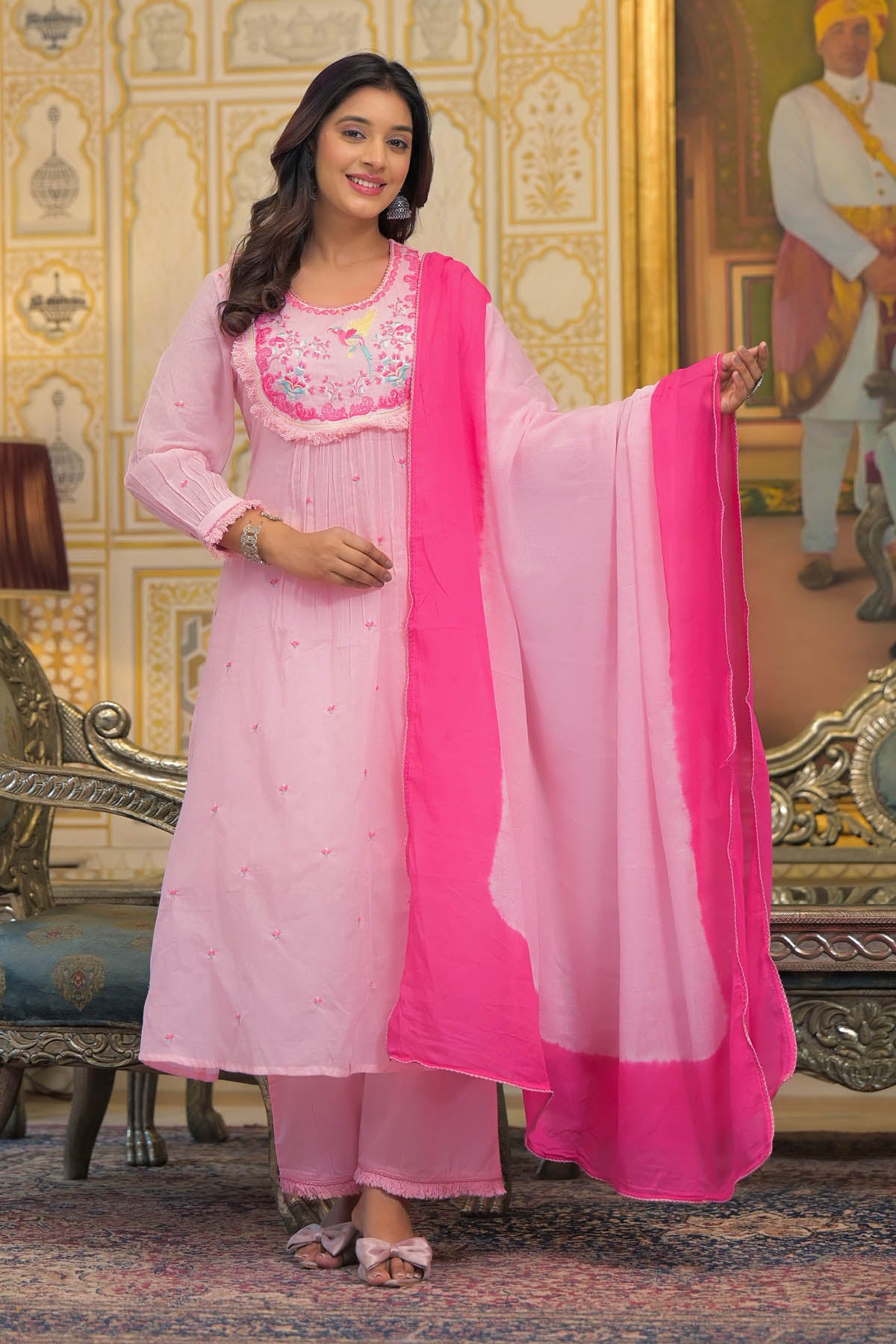 Woman in a pink traditional outfit with a matching dupatta standing in an ornate room.