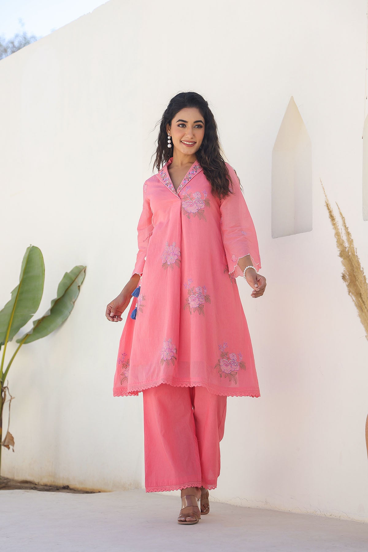 Woman wearing a pink traditional outfit with floral patterns against a white wall.