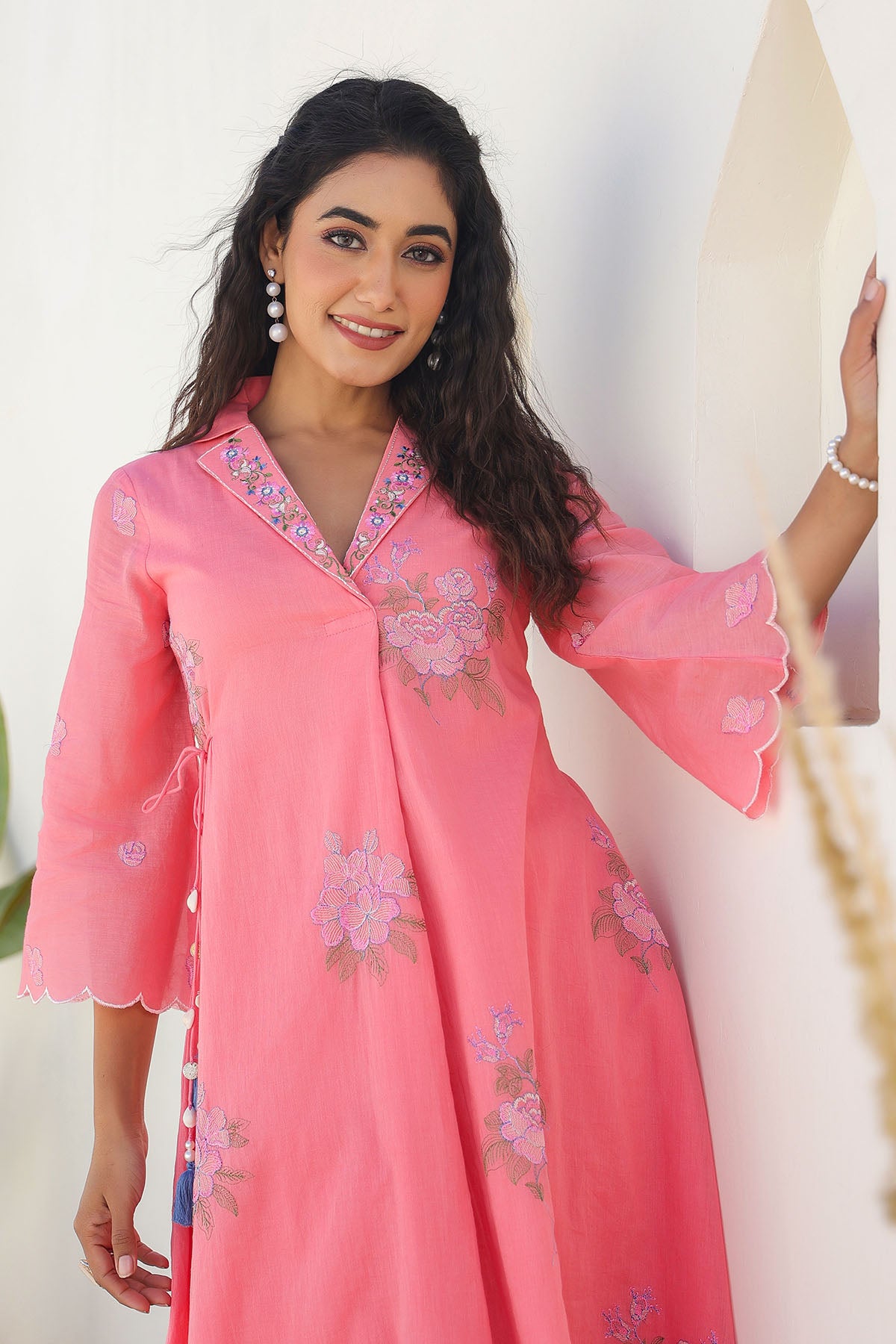 Woman wearing a pink traditional outfit with floral embroidery against a white background