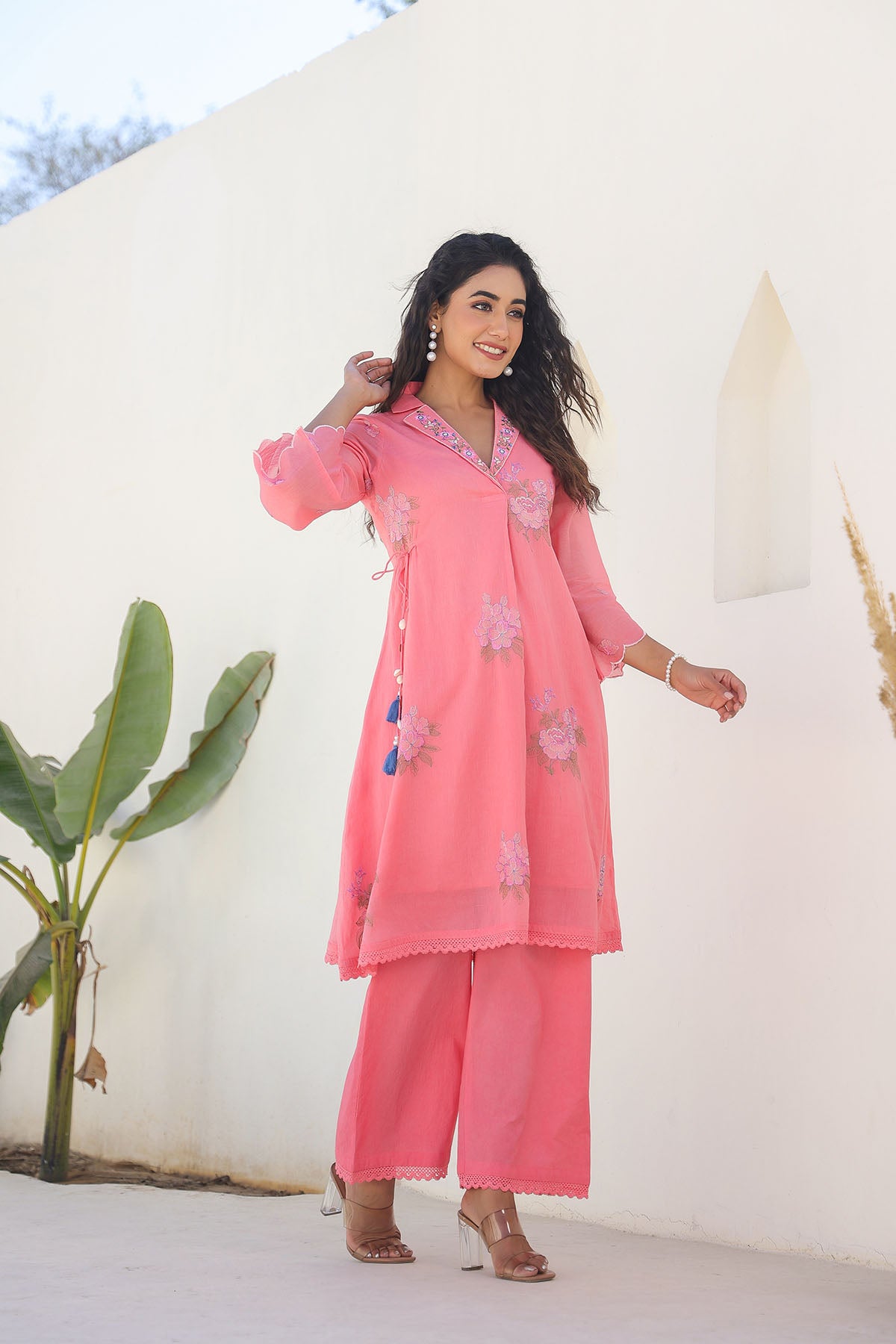 Woman wearing a pink traditional outfit with floral embroidery against a white background