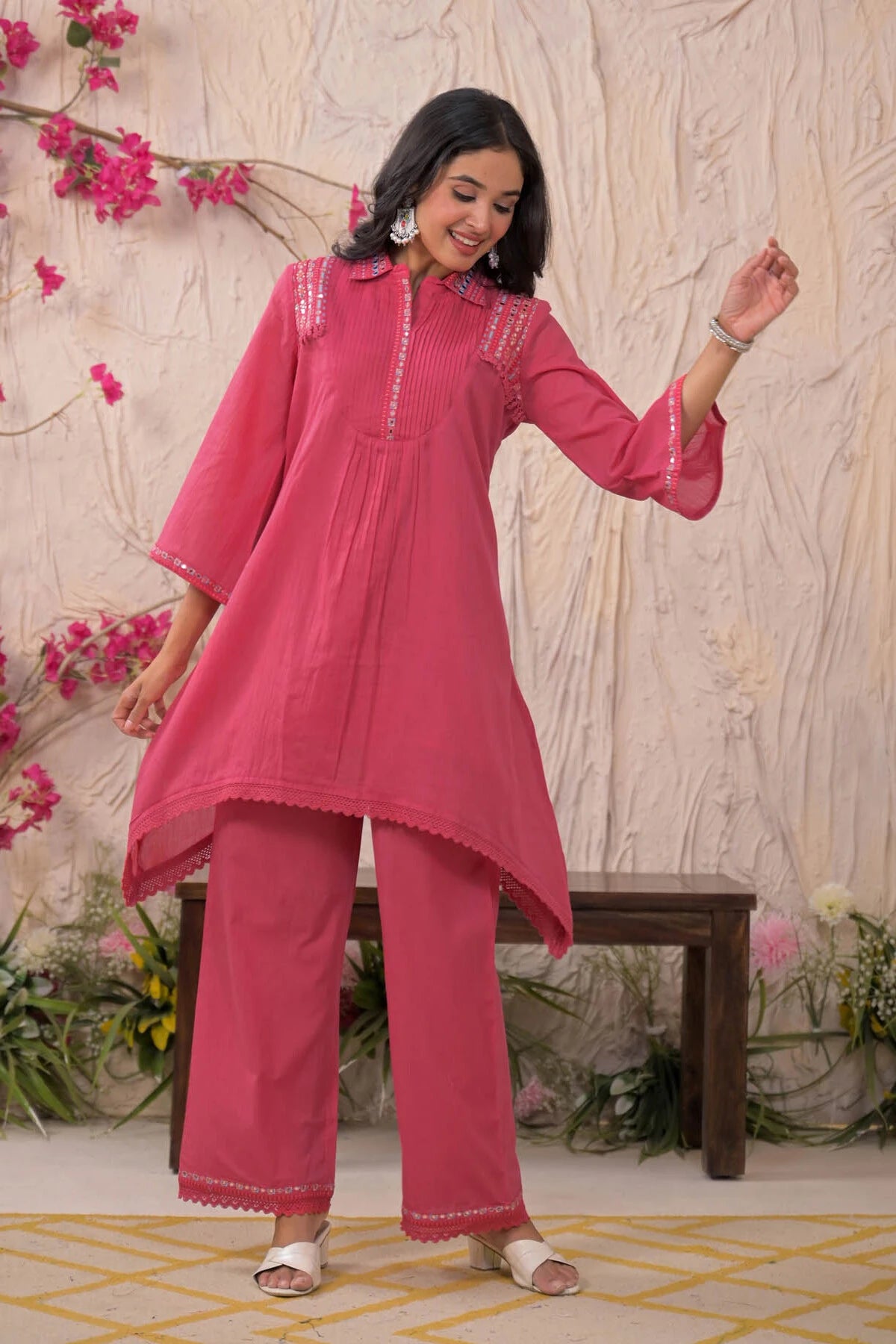 Woman in a pink traditional outfit standing in front of a floral and textured wall.