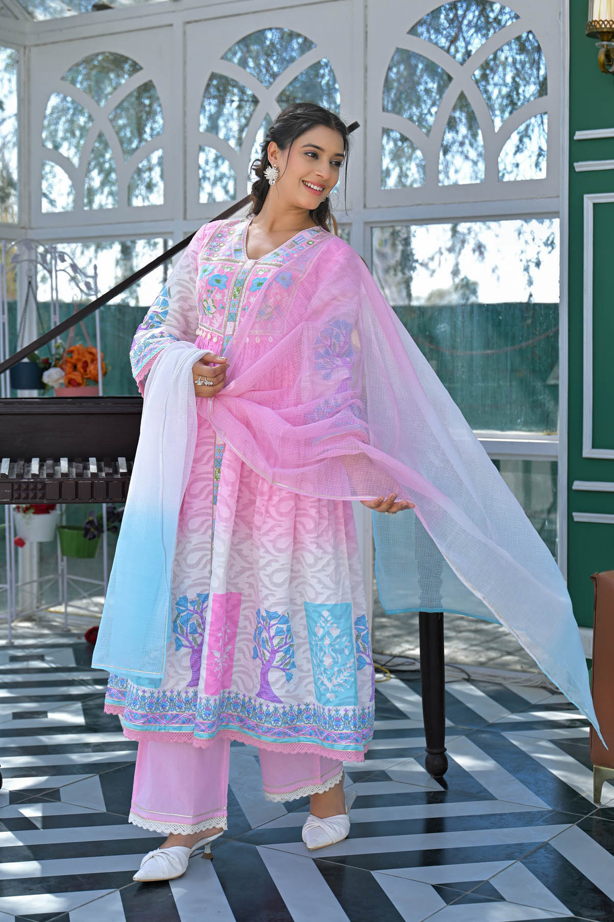 Woman in a traditional outfit with pink and white elements standing indoors.