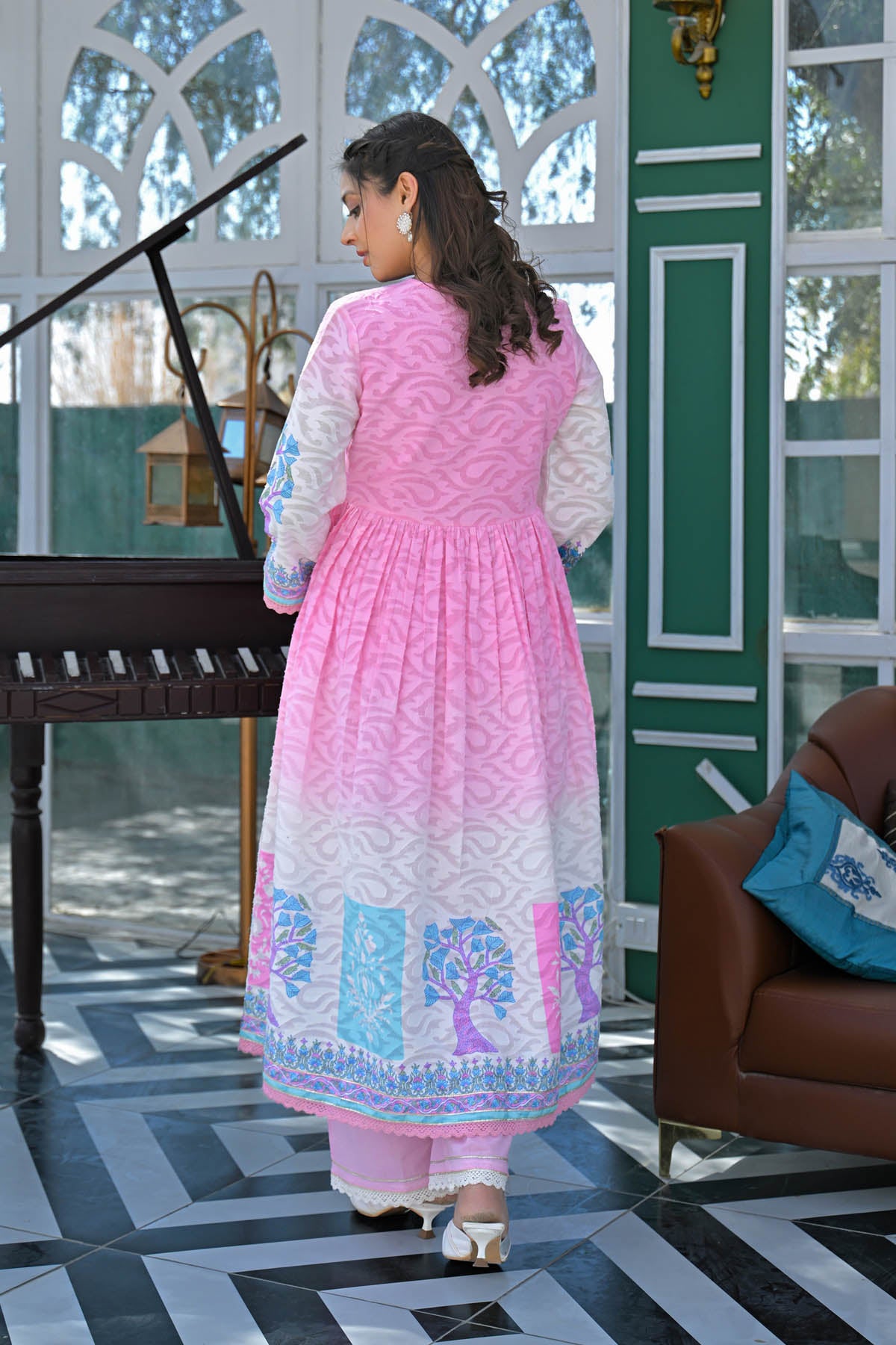 Woman in a pink traditional outfit standing in a room with a piano and sofa.
