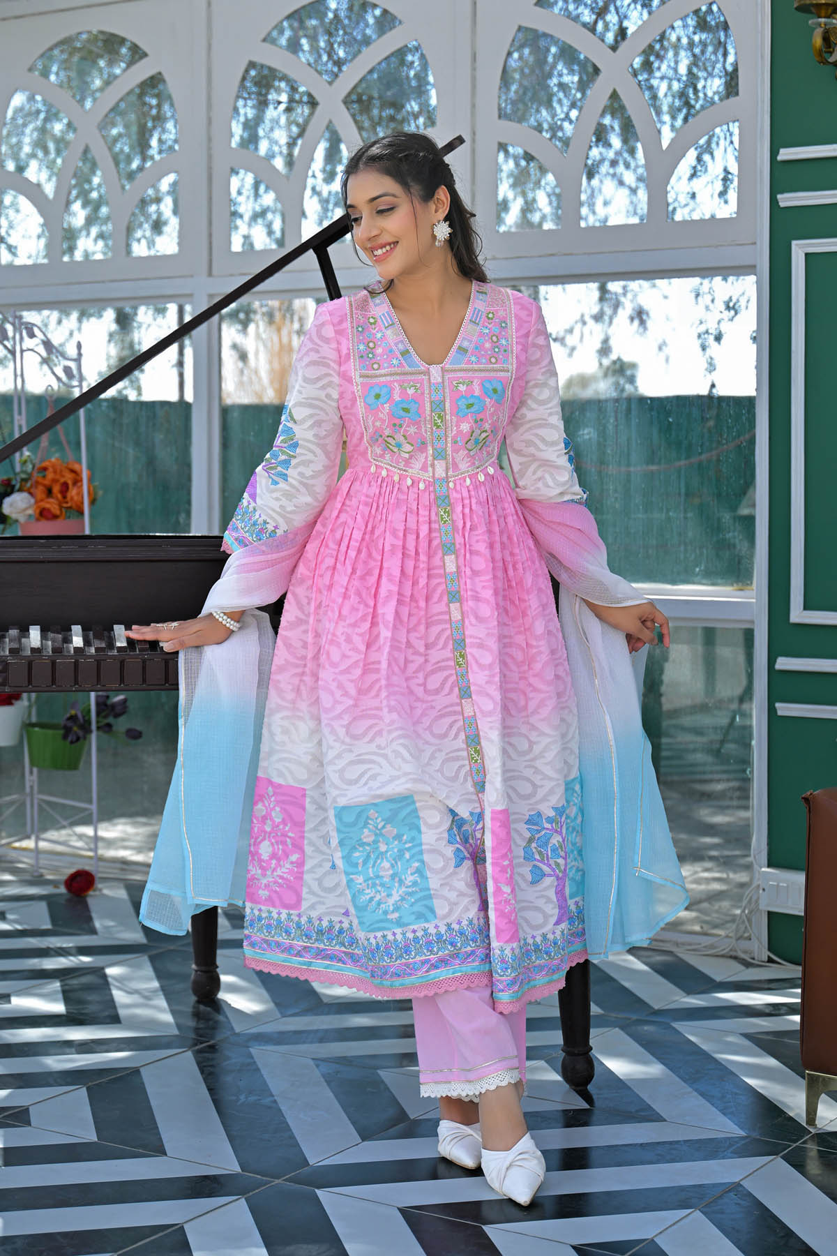 Woman in a traditional outfit with pink and blue patterns standing in a decorative room.