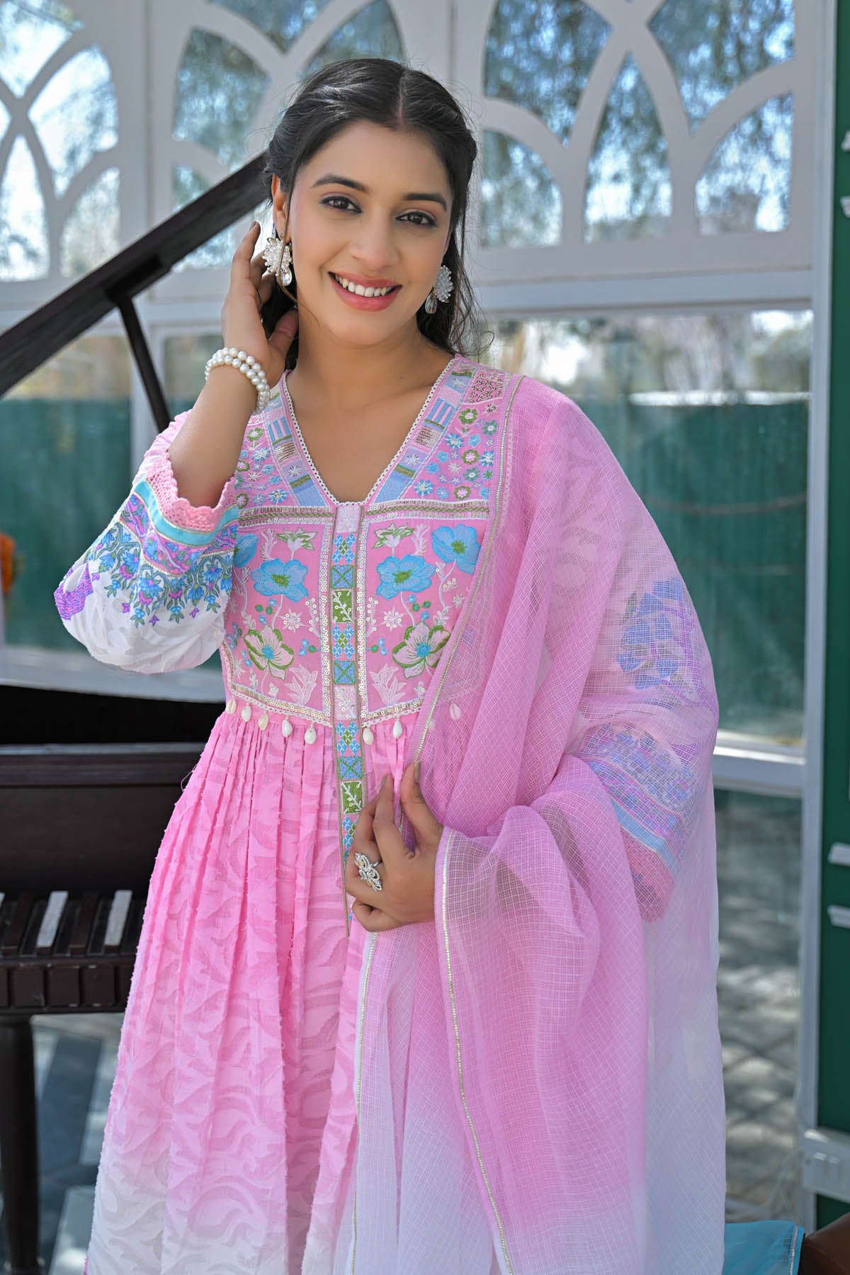 Woman in a pink and white traditional outfit with floral embroidery, standing outdoors.