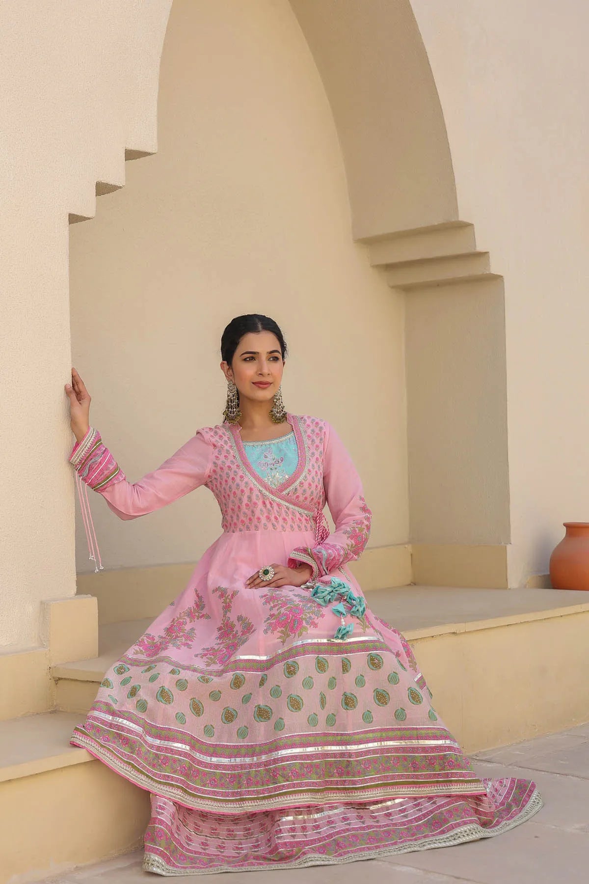 Woman in a traditional pink outfit with intricate patterns standing in an architectural setting.