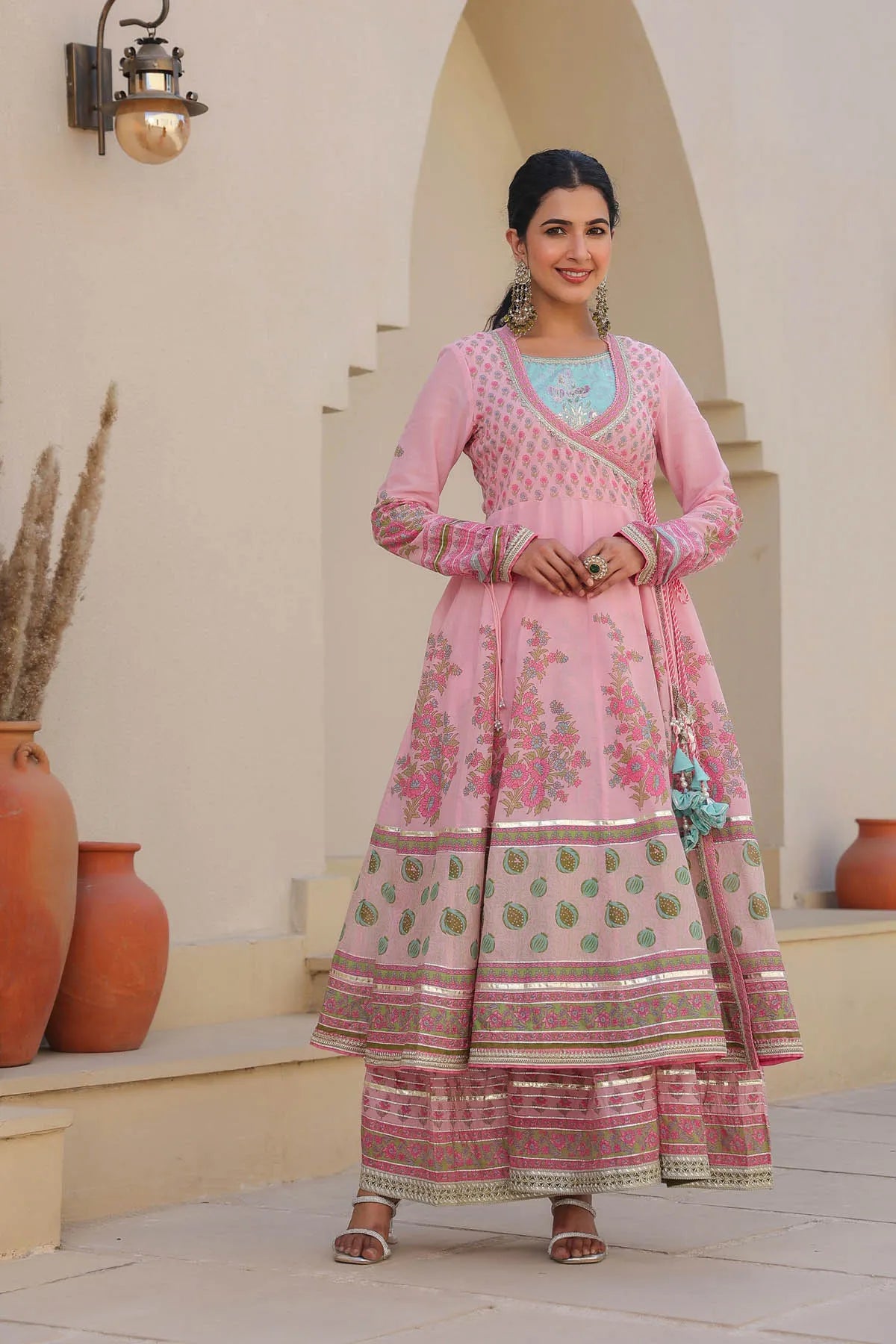 Woman in a pink traditional outfit standing in front of a white wall with decorative pots.