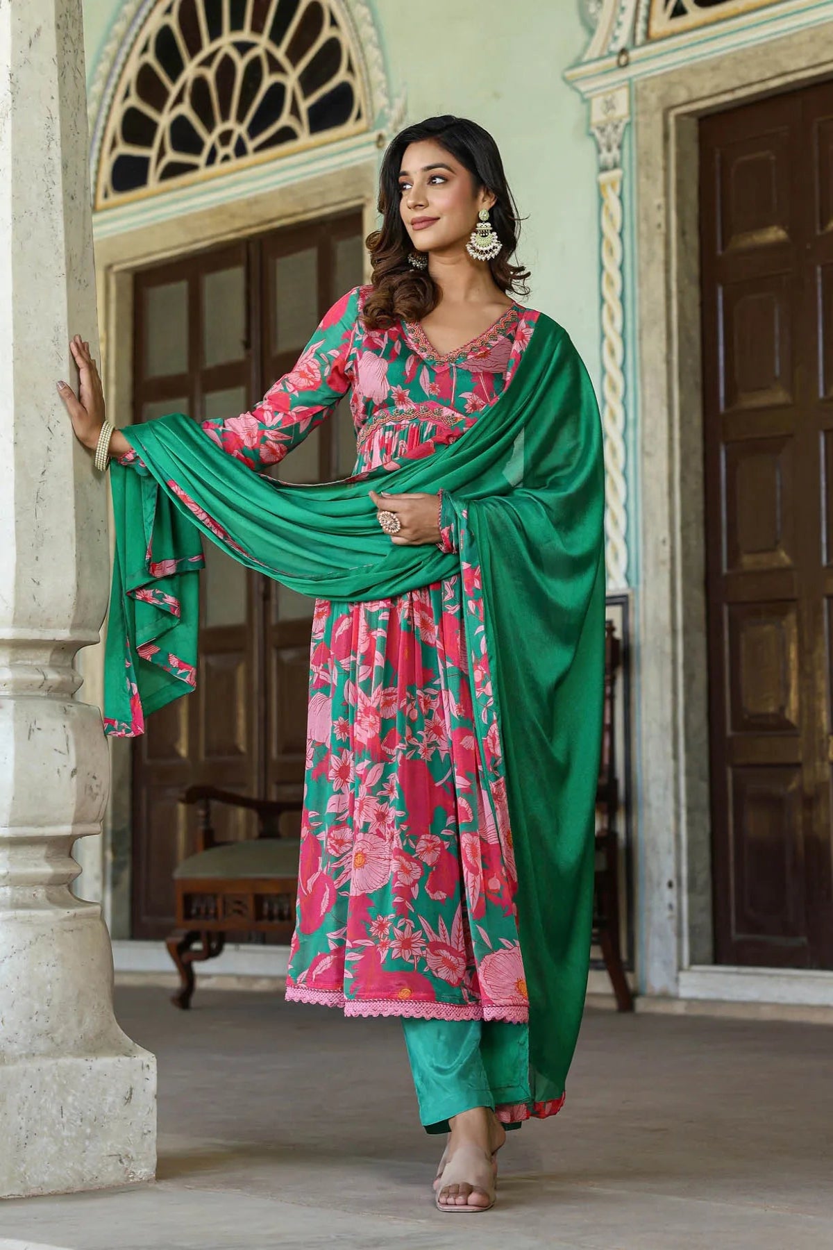 Woman in a green and pink traditional outfit standing in an ornate doorway.