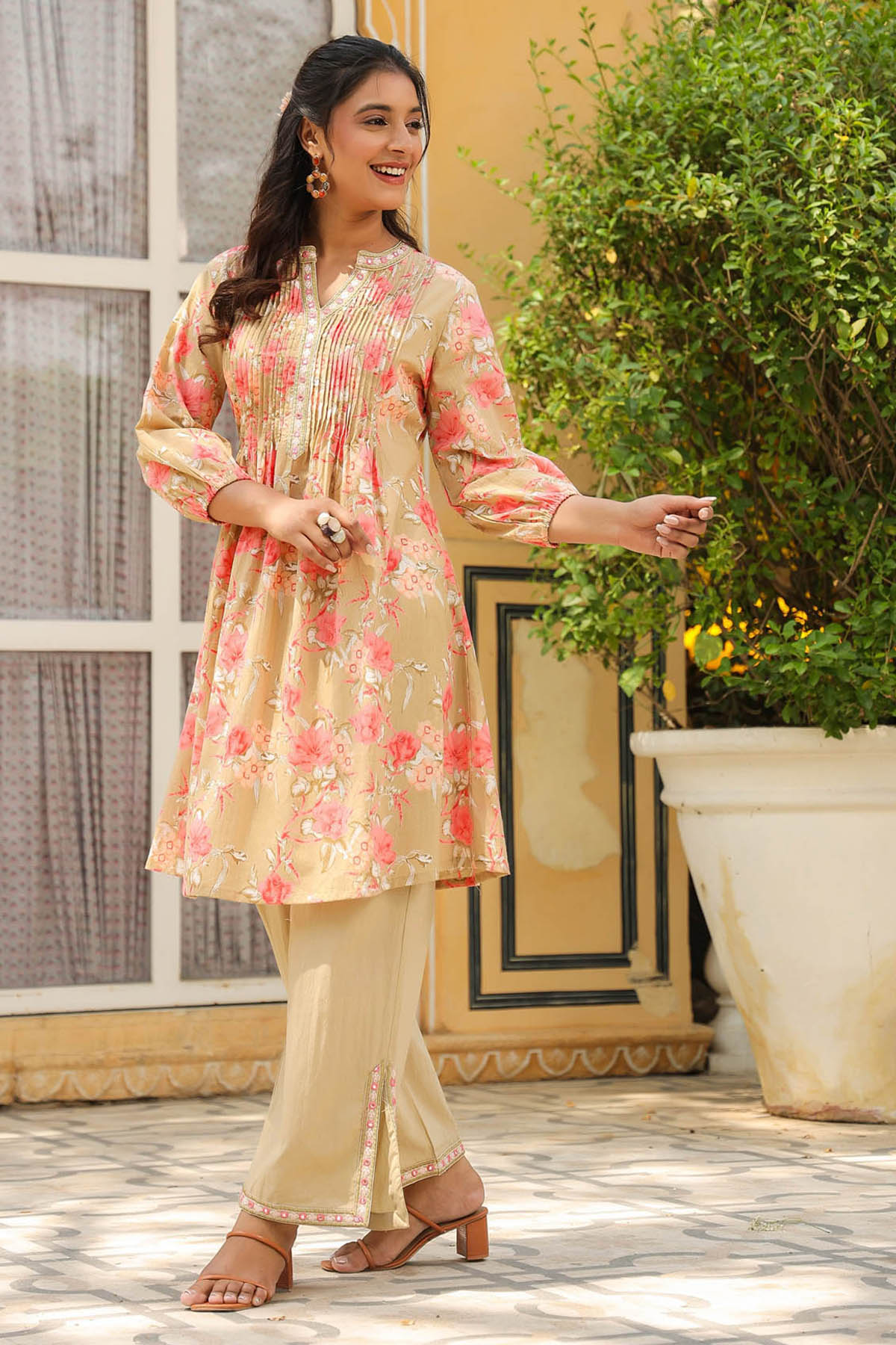 Woman in a floral dress standing outdoors with plants and a window in the background