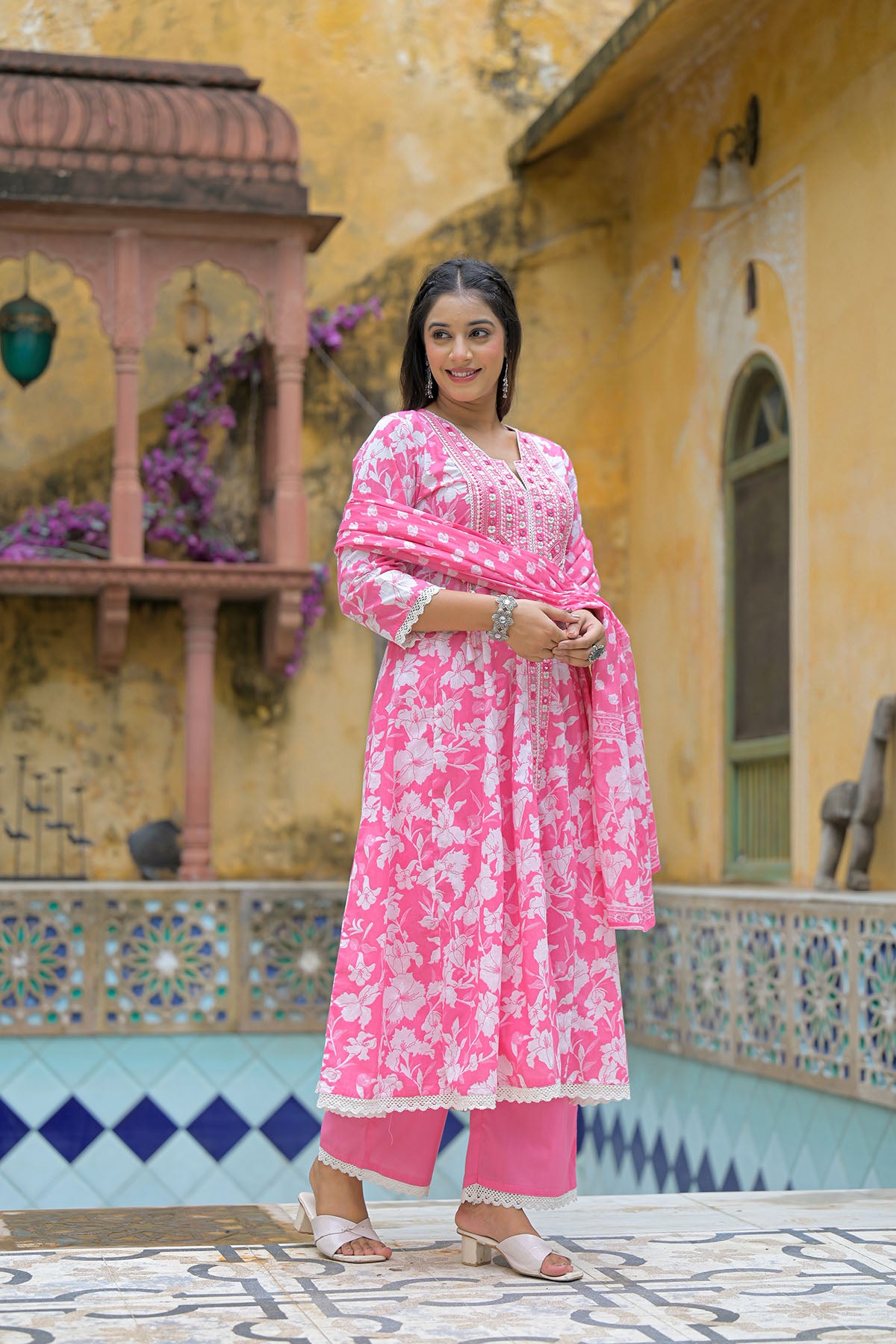 Woman in a pink traditional outfit standing in front of a decorative building.
