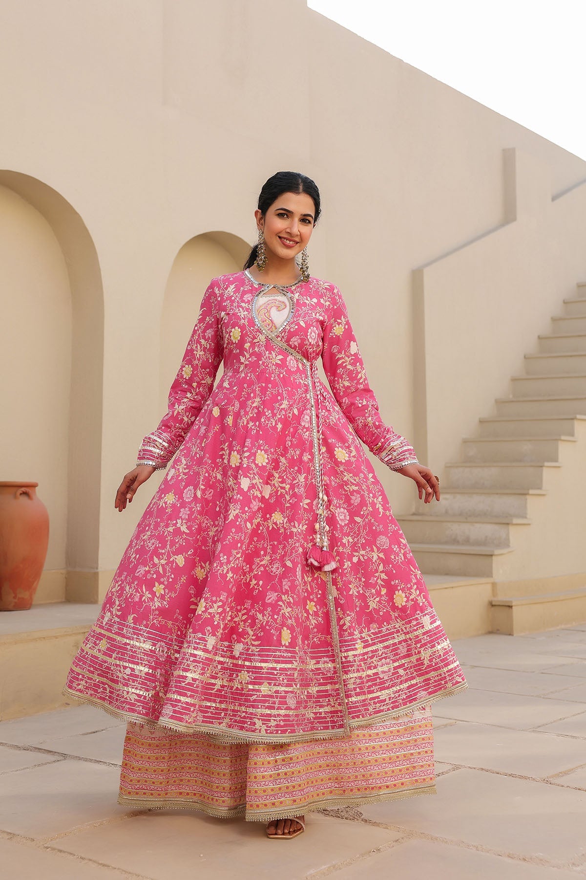 Woman in a pink traditional outfit standing in an outdoor setting with architectural elements.